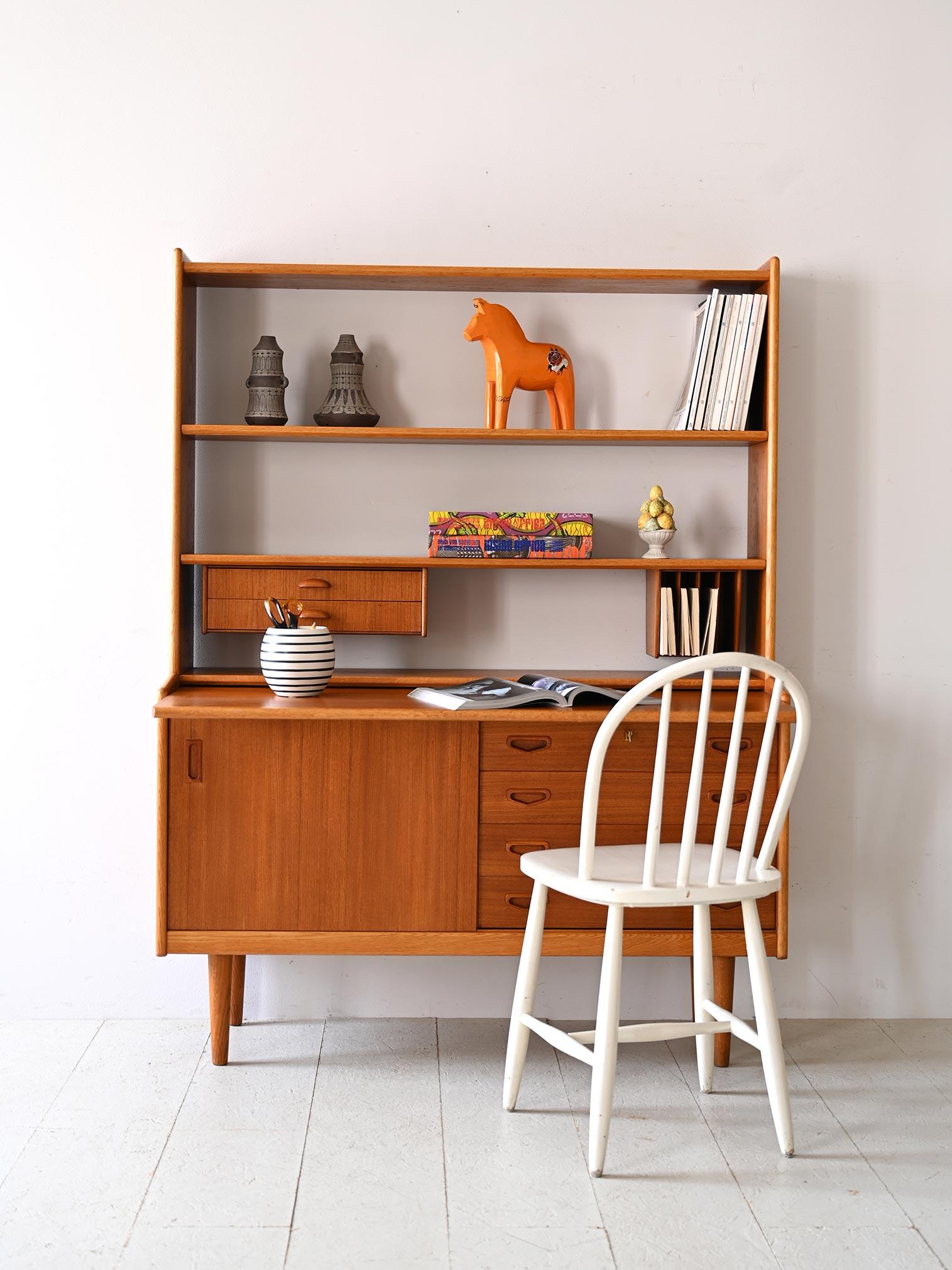 Scandinavian teak bookcase from the 1960s.
The lower part has a compartment closed by a sliding door while the upper part is divided into two sections: two open shelves and two small drawers.
The essential design and clean lines, typical of the