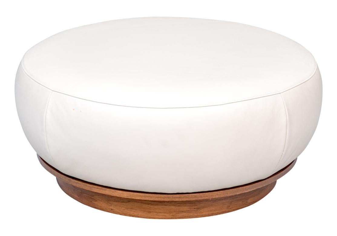 Un ottoman sur mesure  avec un coussin surdimensionné en similicuir sur une base en bois massif tourné. Il s'agit d'une pièce polyvalente qui peut être utilisée comme repose-pieds, siège supplémentaire ou table basse alternative. Fabriqué sur mesure