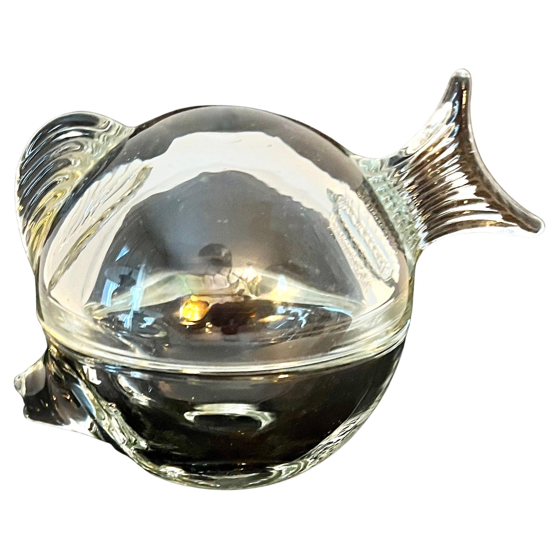 A lovely and unique lidded glass box in the shape of a fish. The piece is basically a sphere of glass with a fin tail and nose of a fish. 

A compliment to a desk or work station to hold paper clips or rubber bands. Also could be used on a