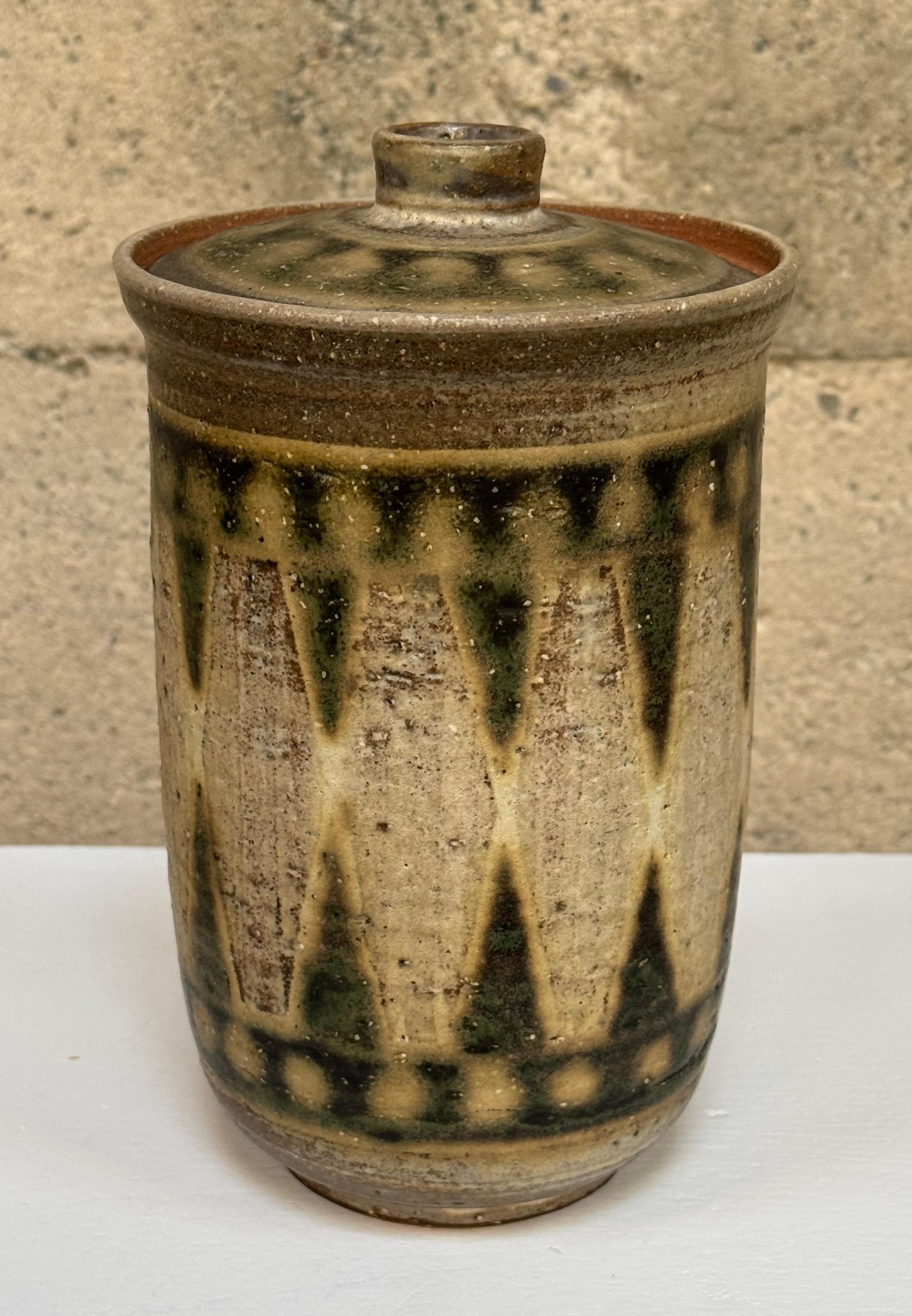 Ceramica da studio con coperchio dell'artista californiano Ernie Kim (1918-1997) forma cilindrica sottile e svasata in alto con un coperchio leggermente affusolato verso il basso, smalti di colore terra con smalti simmetrici.  triangoli e cerchi