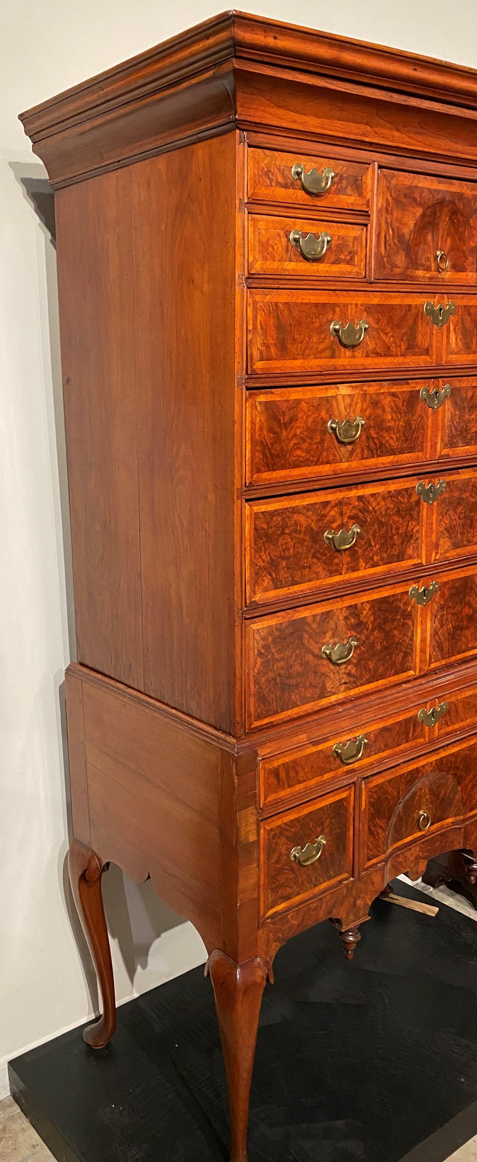 An exceptional two part highboy in burled walnut veneer, the upper case featuring a molded cornice with hidden drawer surmounting a center shell carved deep drawer flanked by two fitted small drawers on either side, and four graduated long drawers,