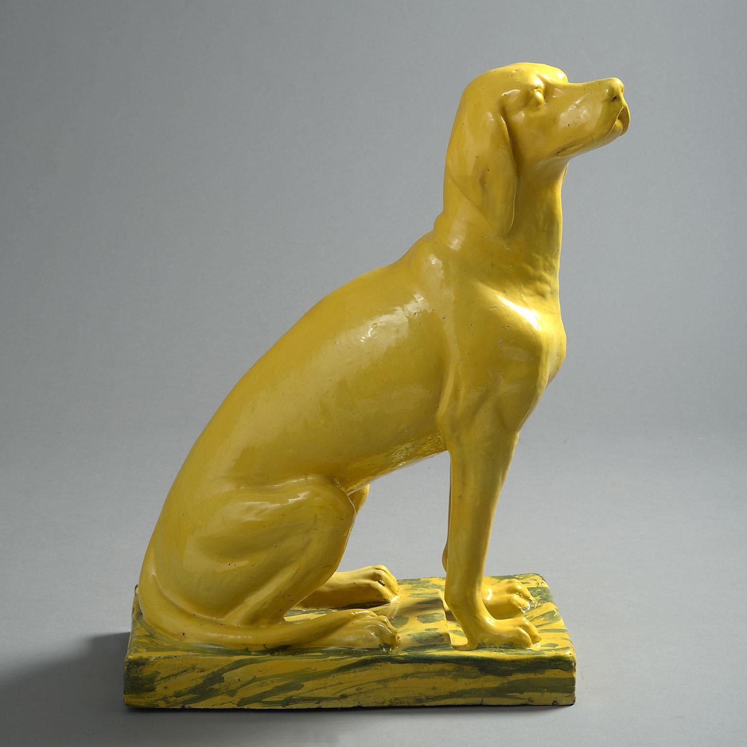 A bright, lifesize yellow glazed canine modelled in a majestic, seated position on a yellow and blue marbled base, the base restored.