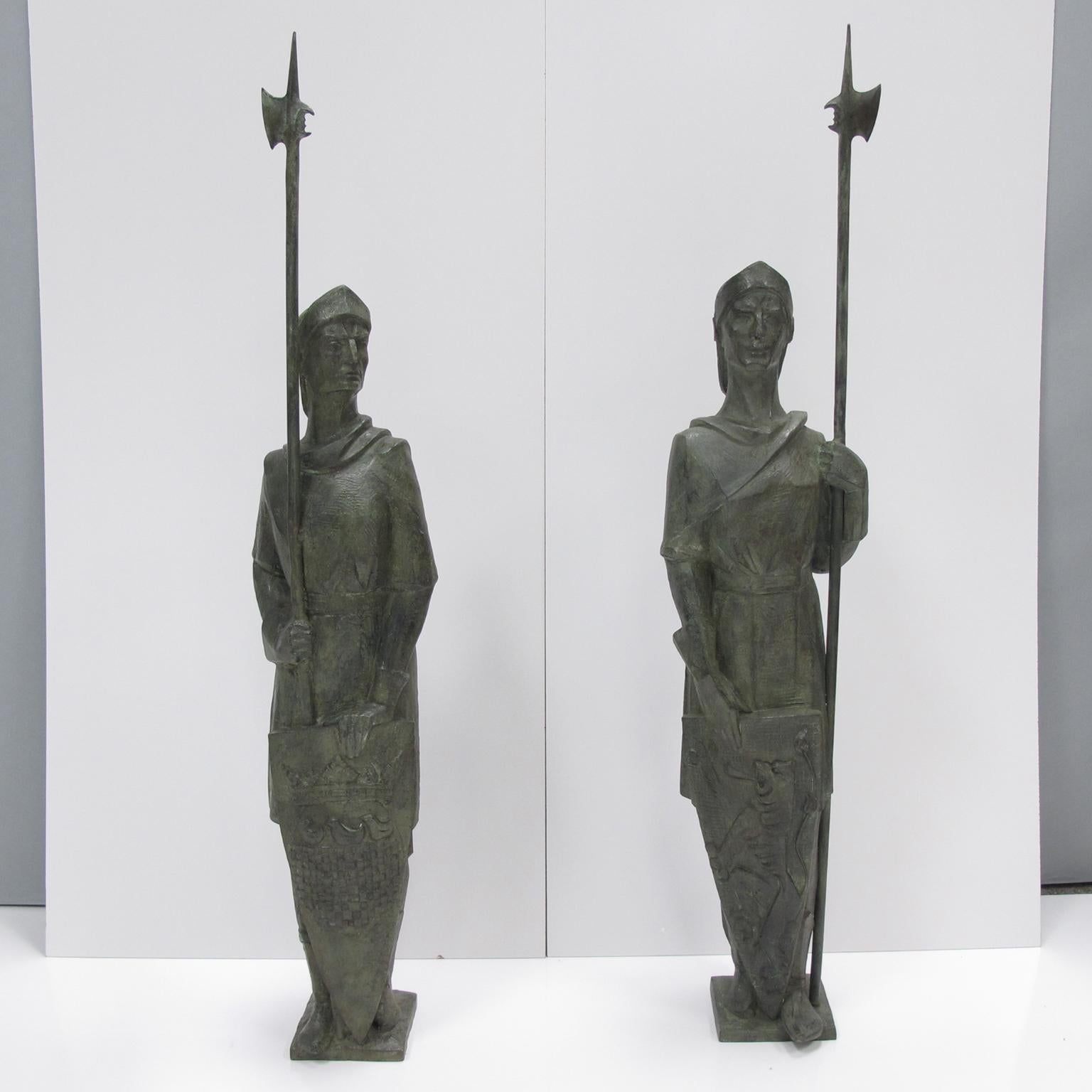 Handsome pair of monumental bronze statues or sculptures featuring antique knights. The signature, located on the base of one piece, is not readable. Impressively detailed design, each knight has a helmet and halbert or spear and a large shield with