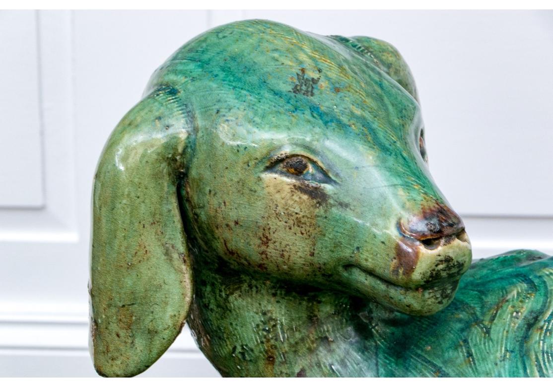 Lebensgroße grün glasierte Keramikskulptur eines liebenswerten, liegenden Lamms. Das Lamm mit gekreuzten Vorderbeinen blickt über sein gut geformtes und plastisches Fell zurück.

Abmessungen: 23 1/2