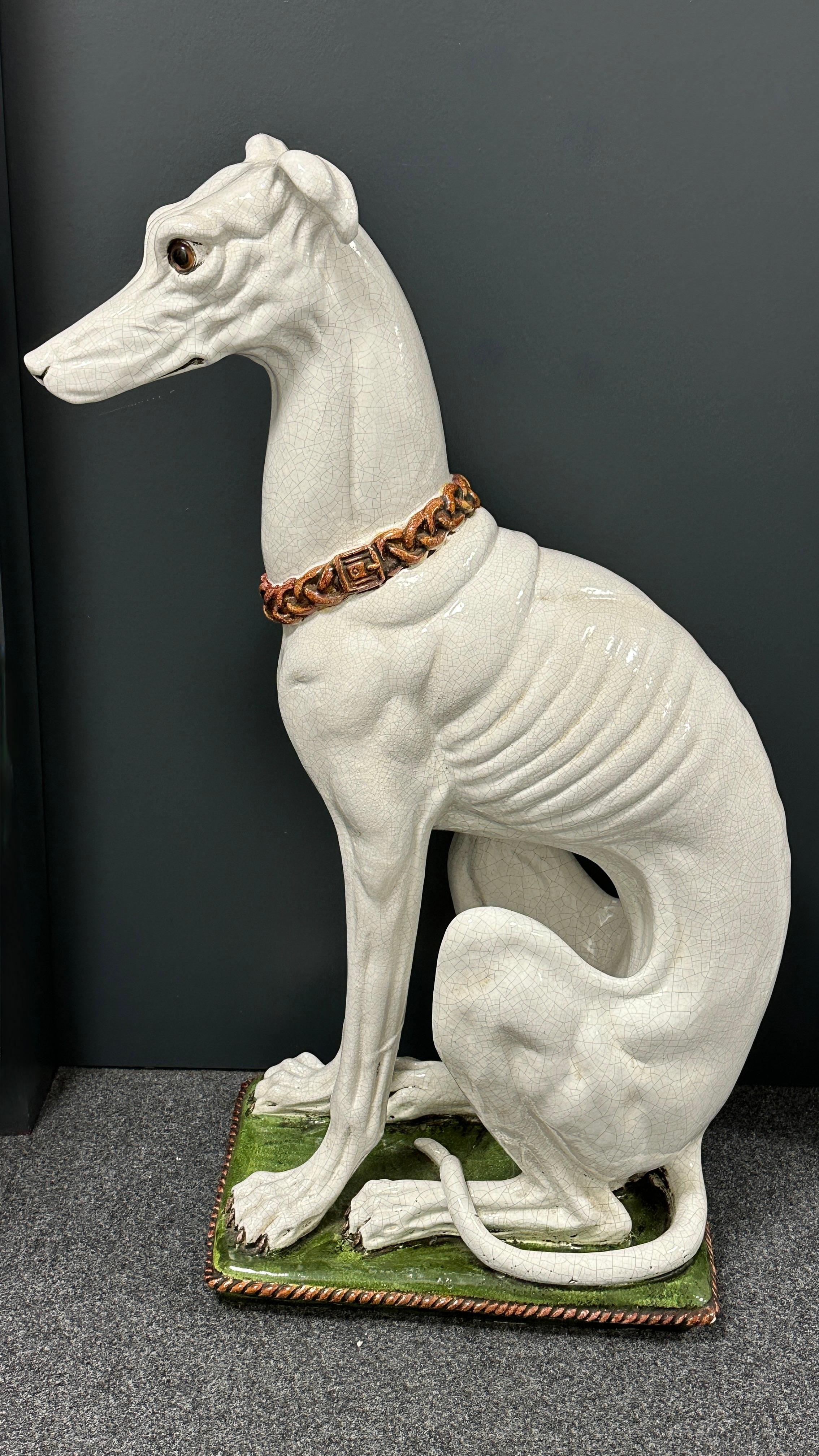 An outstanding Italian Greyhound statue in glazed and hand painted terracotta. Perfectly placed on a pedestal stylized as a cushion, lifelike and life-size representations of this majestic being, stern, watchful and obedient at the same