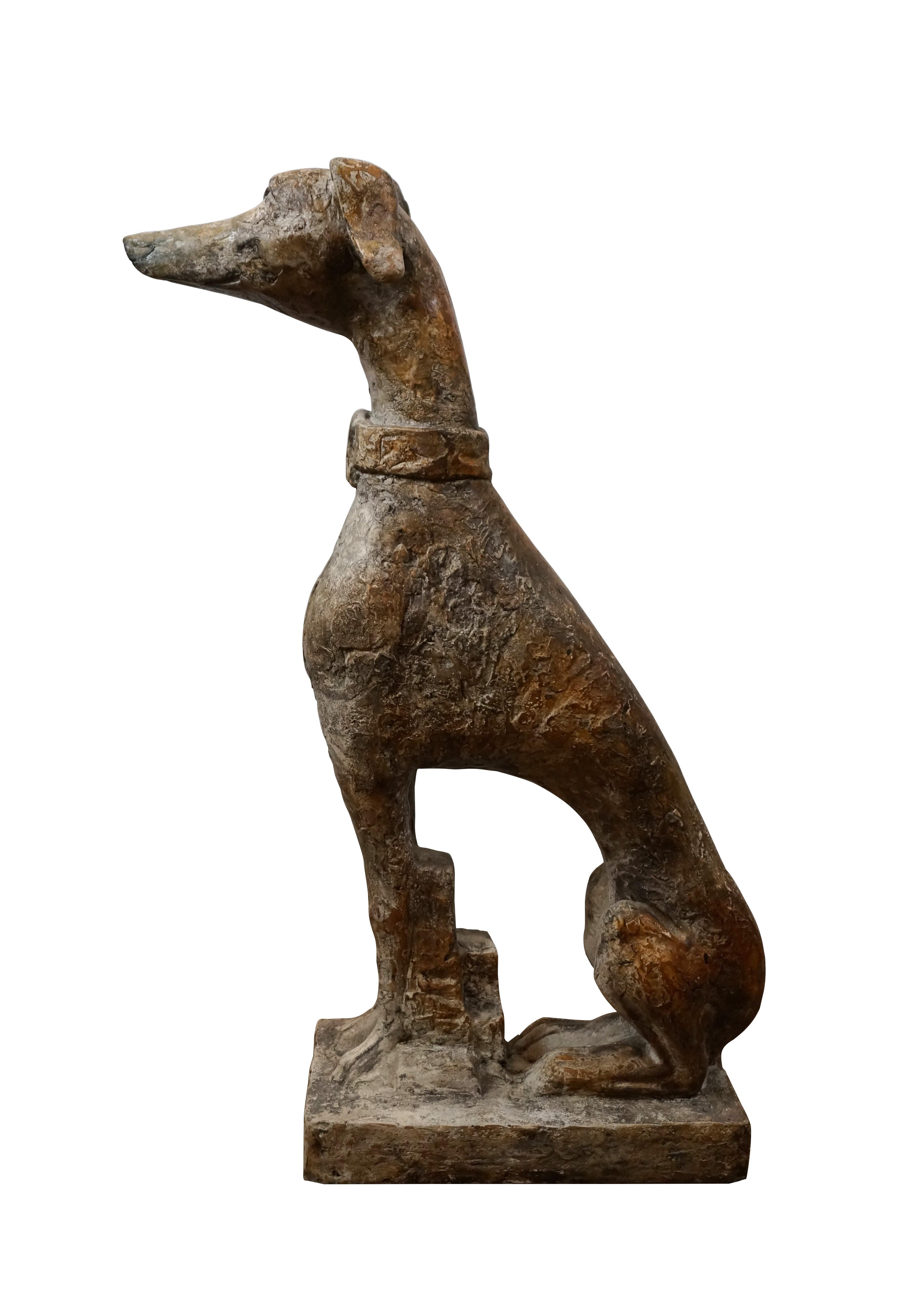 Escultura de composición de tamaño natural de finales del siglo XX que representa a un galgo italiano o whippet con collar ancho, sentado atentamente sobre una base rectangular. Acabado rugoso marrón moteado. No es resistente al agua - sólo para