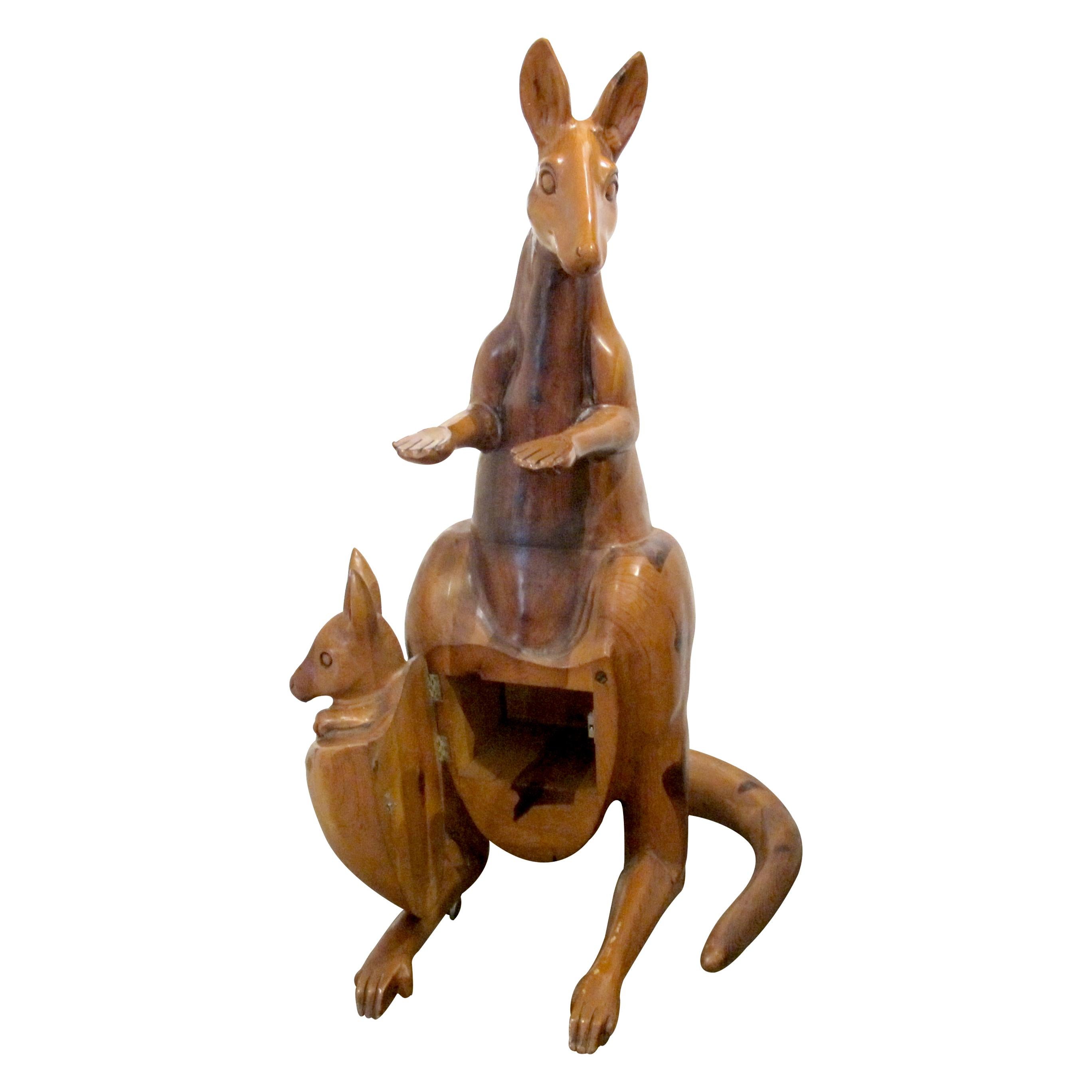 A life-size sculpture of a kangaroo, expertly hand-carved from warm-toned oak, dating from the 1960s, Spain. The piece features a mother kangaroo with outstretched forearms and a charming joey peeking from her pouch. The joey’s compartment opens on