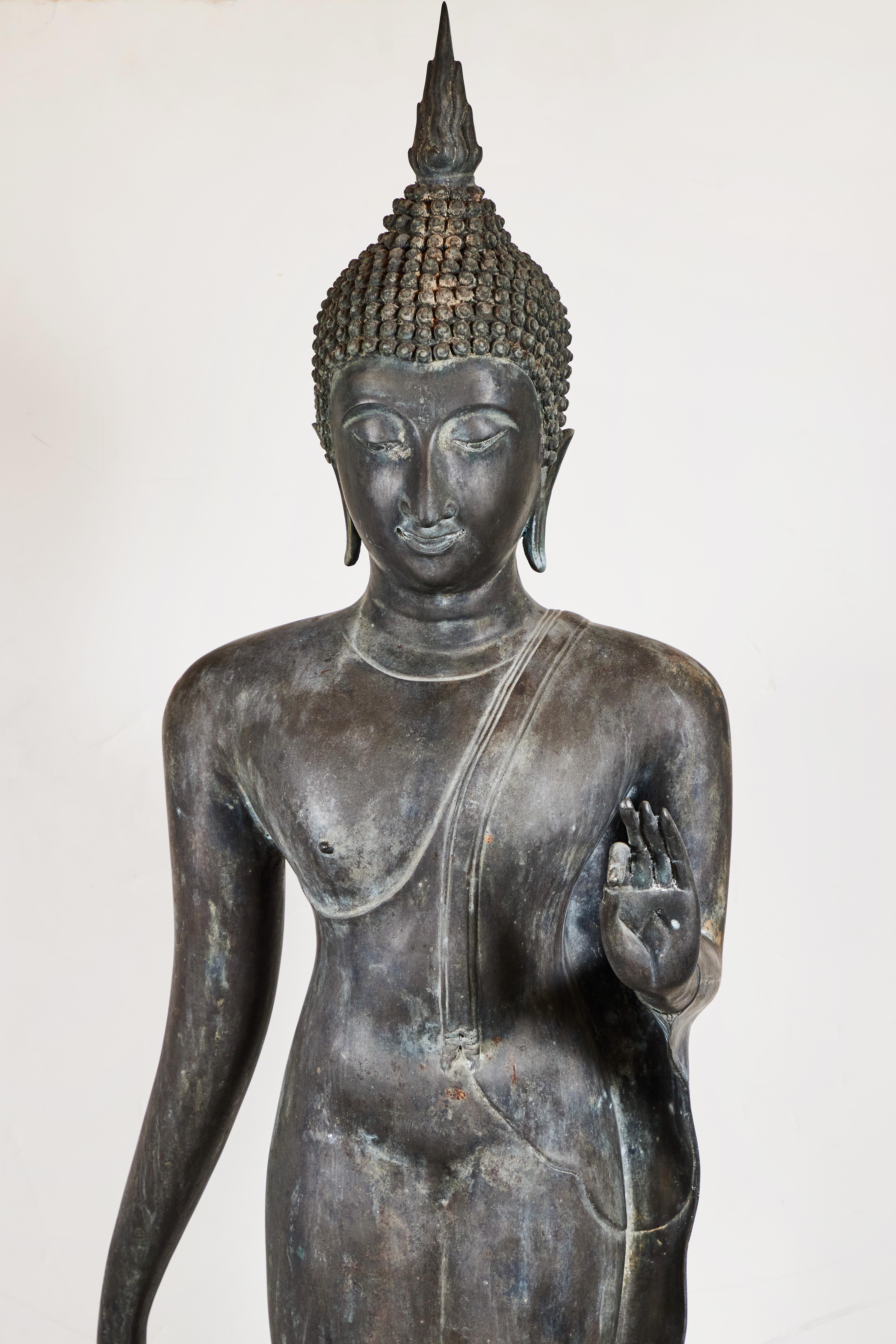 A beautiful, circa 1920, cast bronze Buddha in mid-stride atop a stylized lotus blossom. The figure is clad in  see-through drapery, and is surmounted by whirls of hair capped with a finial, symbolizing the flame of illumination. This Buddha makes