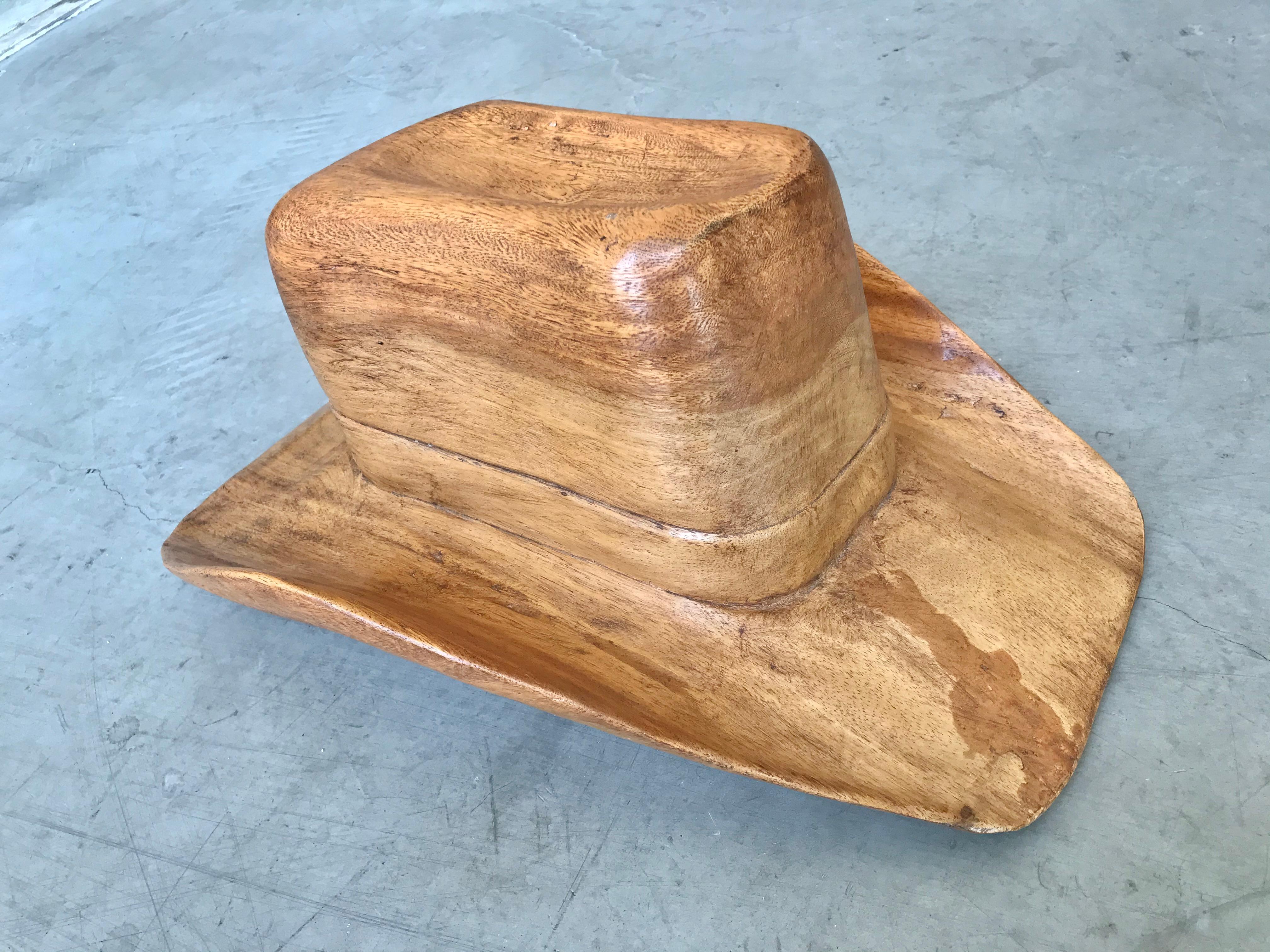 Rustic hand carved wood cowboy hat. There is a carved belt buckle on one side of the hat and a carved sash around the brim of the hat. Fantastic piece of Folk Art. Excellent workmanship. Large scale.