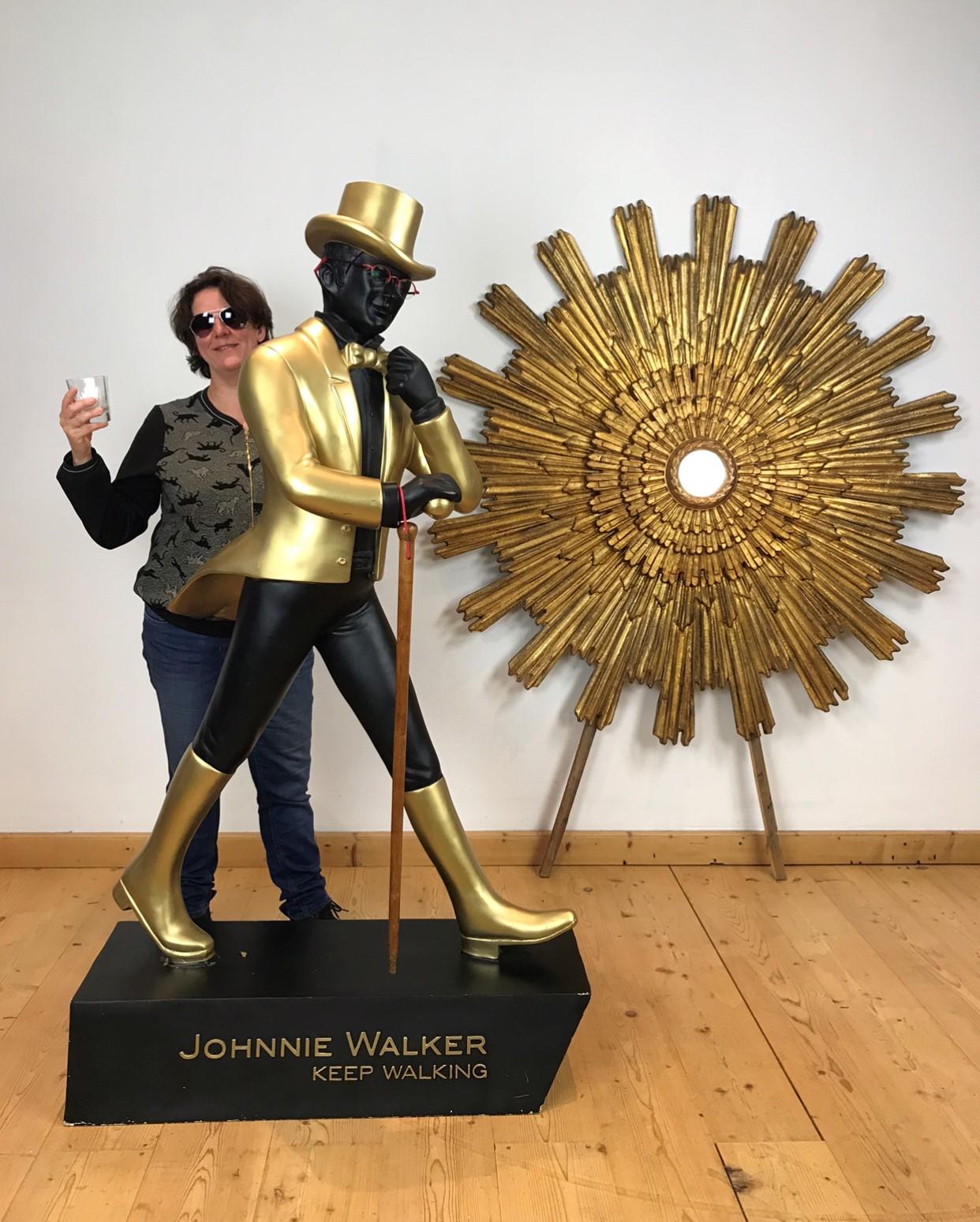 Lifesize Johnnie Walker display man.
A lifesize advertising display - shop display - store display figure for Scotch whisky. 
The typical striding man with top hat, coat, boots and walking stick.
A black and gold advertising figure for the