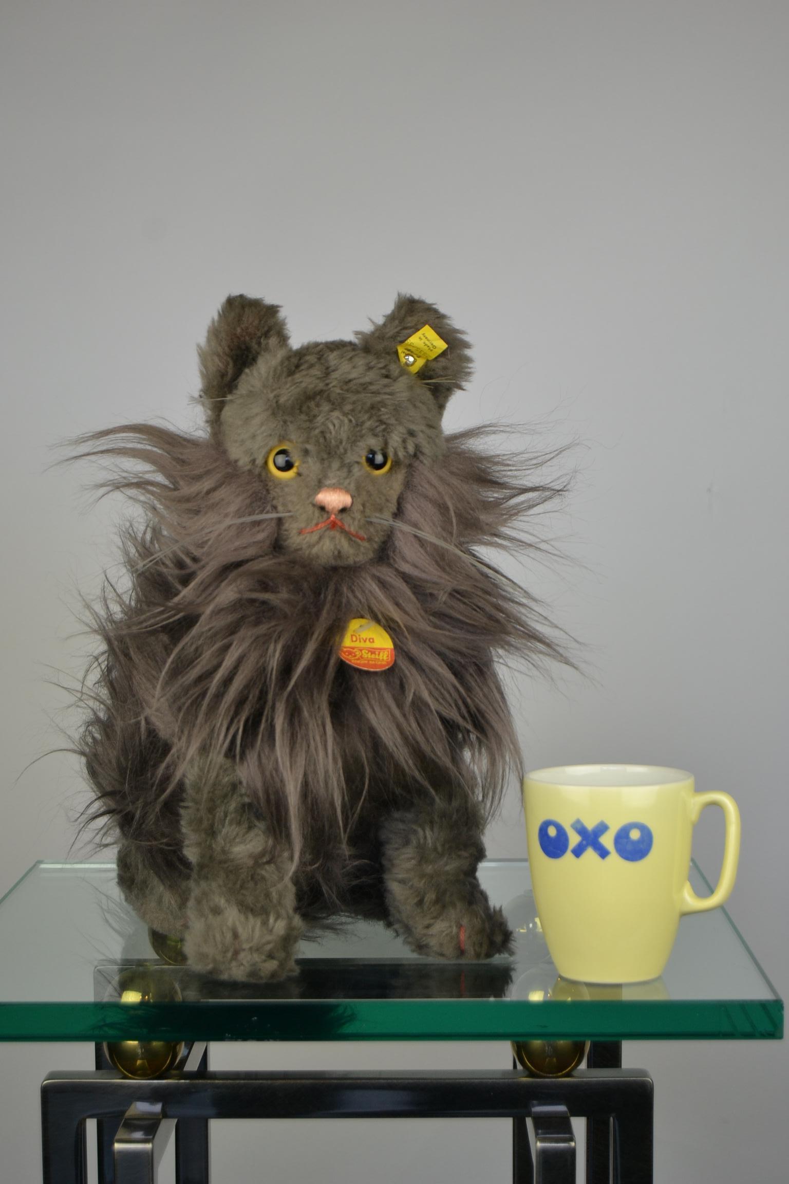 Gray sitting Persian cat toy doll called Diva.
Lifesize vintage toy cat with rotating head and bow around the neck.
Made from 1968-1978. Complete with label and button in the ear and label on the neck. Numbered 2835/35. 

Great home decor for