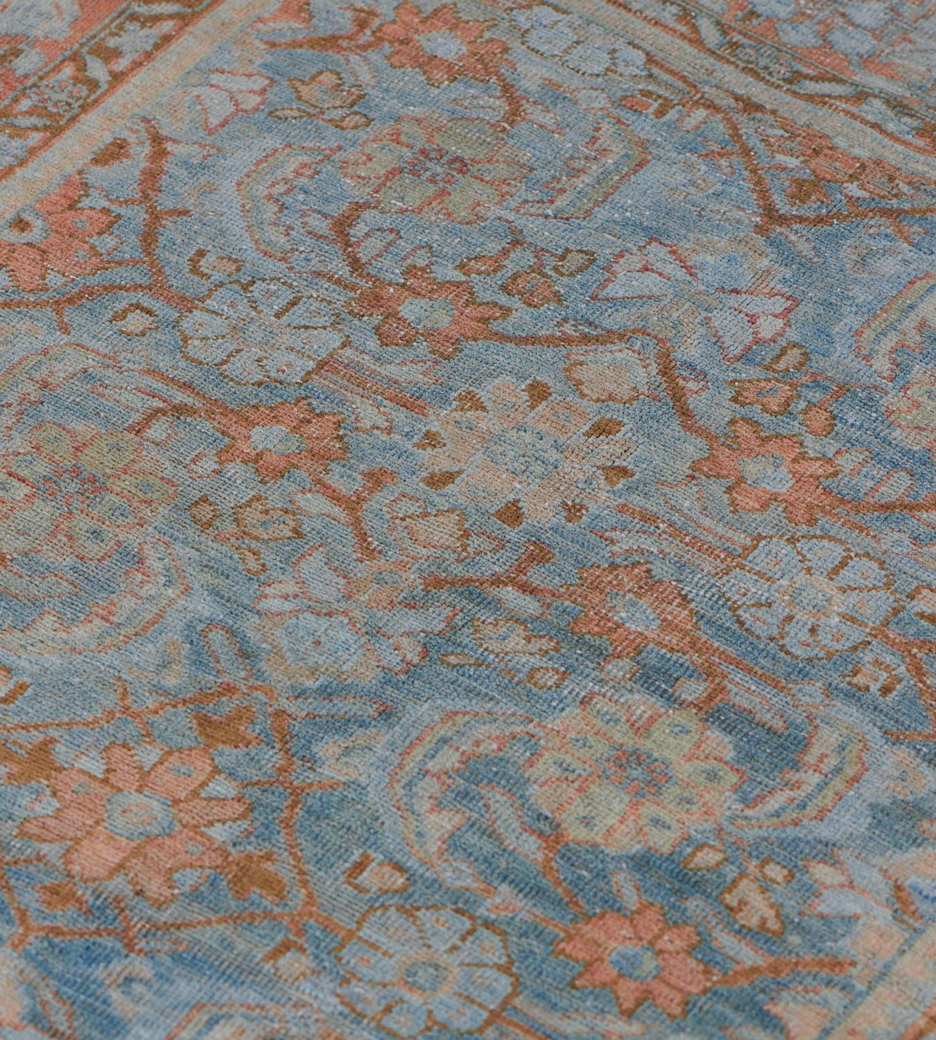 Questo tappeto Mahal antico, risalente al 1920 circa, ha un campo blu chiaro con un motivo herati rosso mattone e marrone buffo, con un bordo rosso mattone con palmette angolari a meandri e foglie di vite blu chiaro, tra strisce floreali marroni
