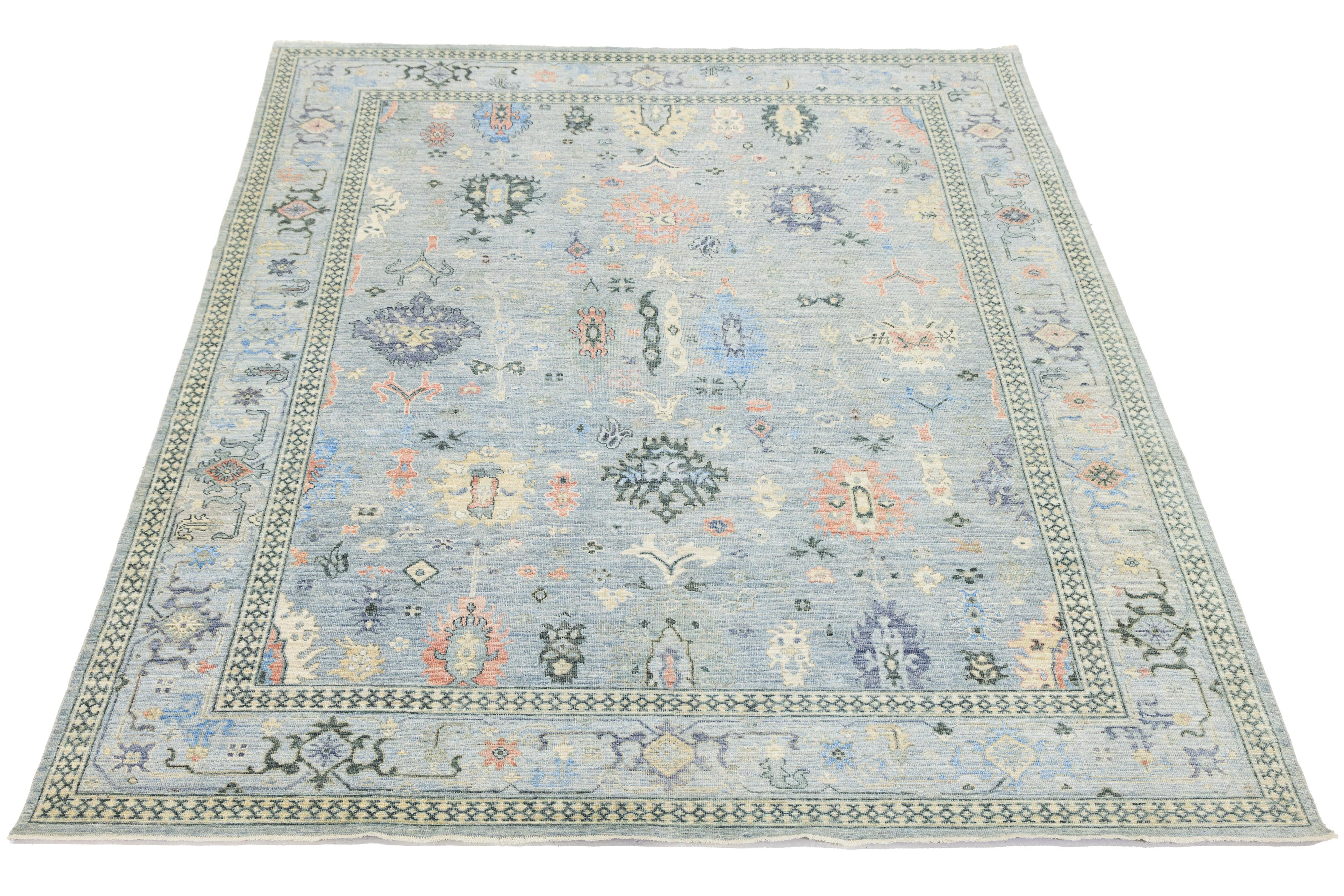 Ce tapis moderne en laine de style Oushak, noué à la main, présente un fond bleu clair avec des motifs floraux. Le design fusionne l'esthétique contemporaine et l'artisanat traditionnel d'Oushak. Les couleurs et les motifs peuvent contribuer à