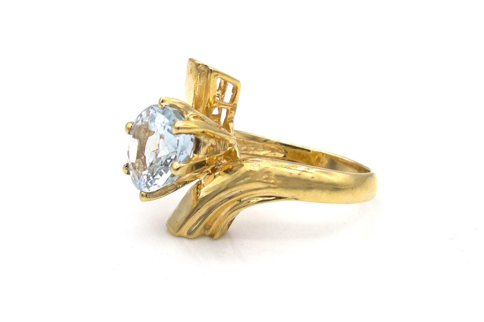 This original Ben Moses ring has a 14 karat yellow gold band that twists around the finger, featuring a unique, yet elegant modern design and an off-set light blue oval-cut Topaz at the center. The Topaz weighs in at approximately 3 Carats total.