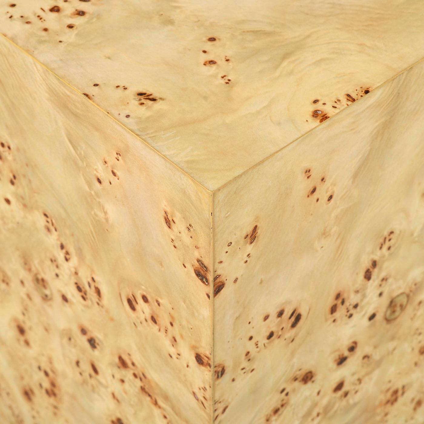 Conçue avec des lignes épurées et modernes, cette table de forme cubique est enveloppée d'un luxueux placage de ronce de mappa au poli brillant transparent, mettant en valeur son grain de bois complexe. La base est rehaussée d'un socle en laiton