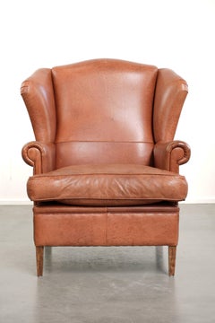 Sillón inglés tipo «wingback» de color coñac claro, fabricado en piel de vaca