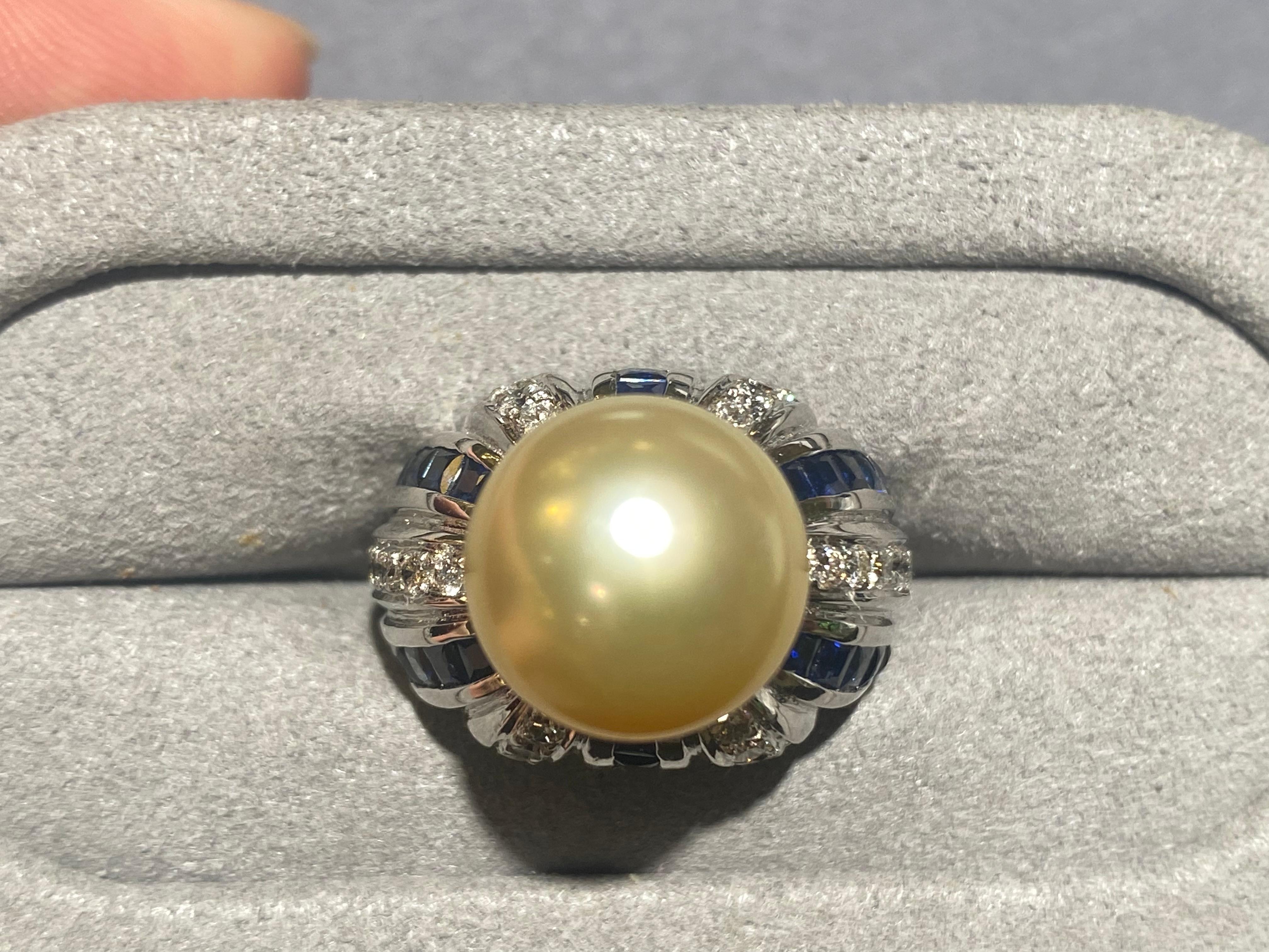 A 12.5 mm light golden South Sea Pearl, diamond and sapphire Ring in 18k white gold. The pearl is sitting in the middle of the ring and pave of diamonds and sapphire is radiating our from the base of the pearl. The pattern of the diamond and