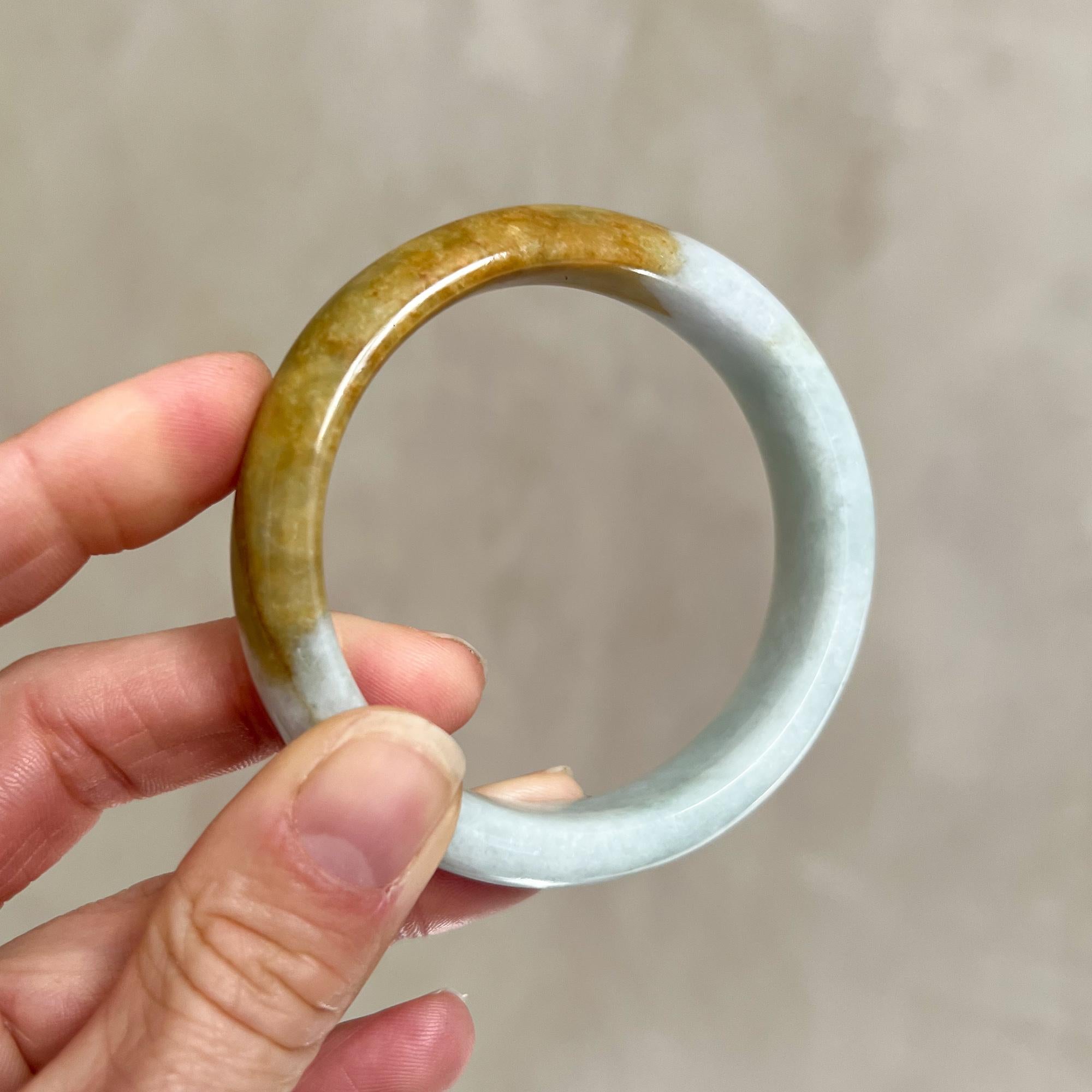 A natural jadeite jade light greenish grey and partly brown mottled untreated bangle bracelet. The bangle is small in size and measures 60 mm inner width and band width 15 mm. The outer diameter is approximately 75 mm and depth 9 mm. The bangle has