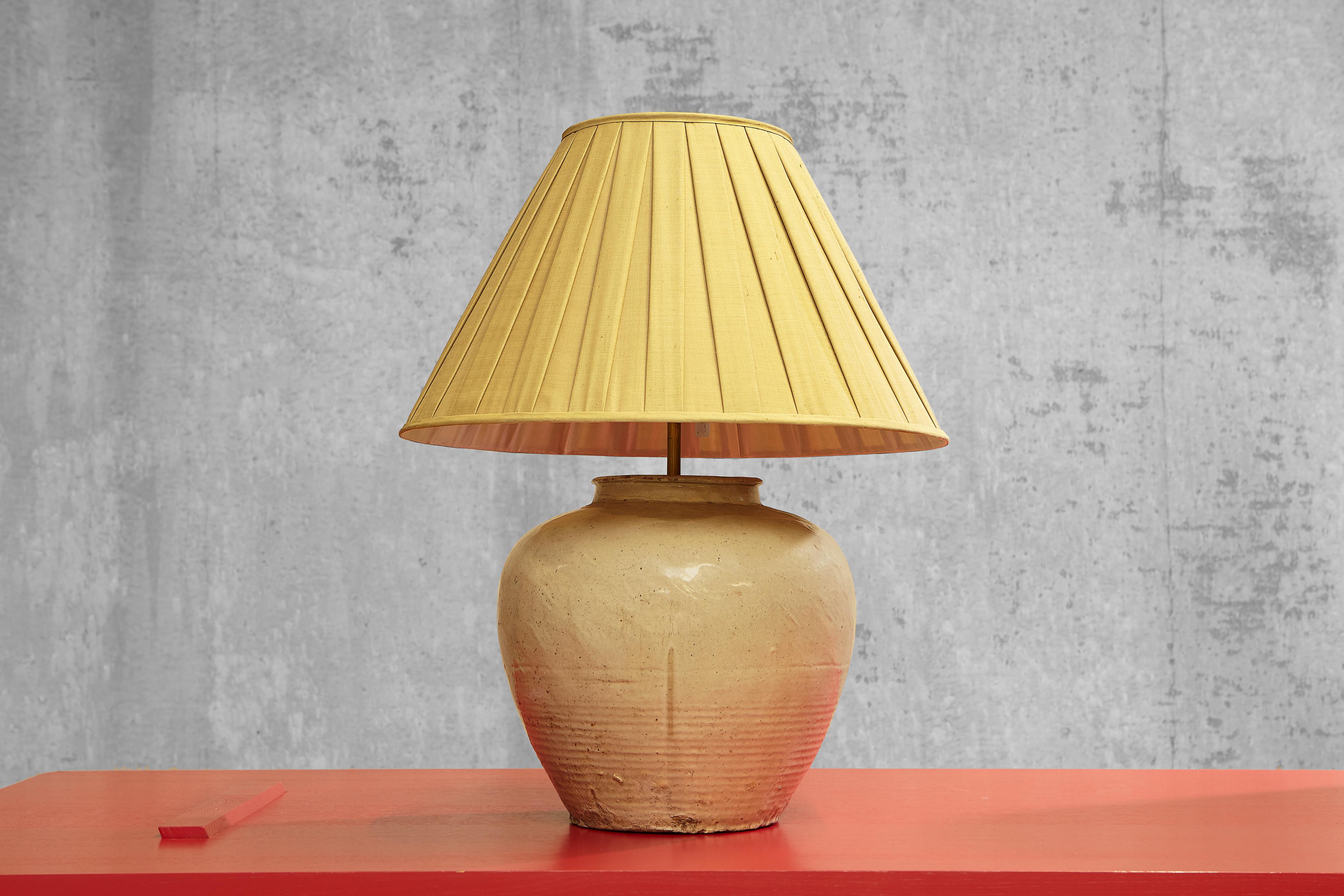 Cette magnifique lampe de table est fabriquée en poterie émaillée chinoise et présente des tons gris clair et sable. La lampe en poterie émaillée de forme ronde attire l'attention de manière simple mais élégante. La poterie émaillée est un matériau