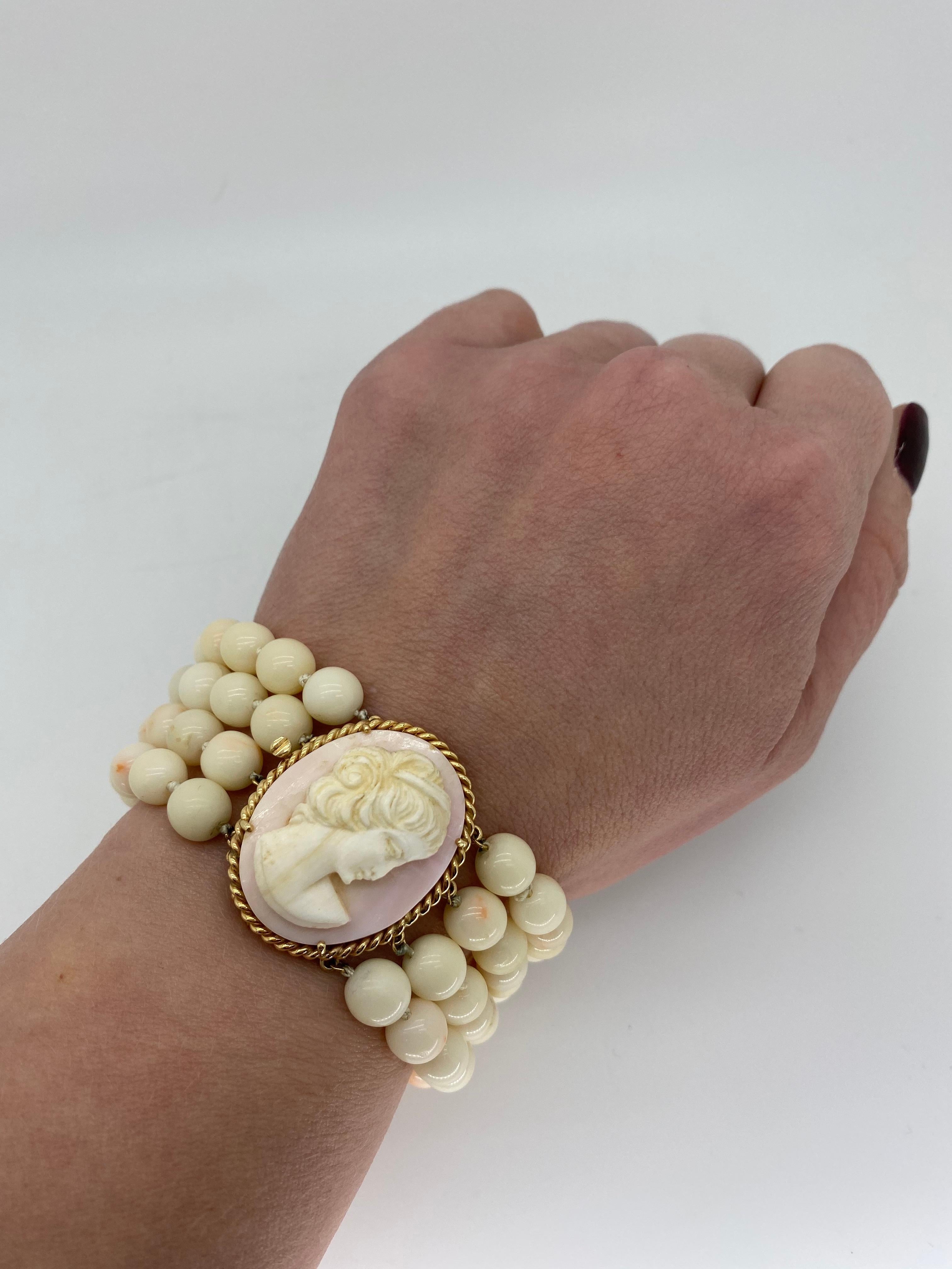 Four strand cameo and coral bead bracelet with a uniquely crafted 14k yellow gold clasp.

Gemstone: Coral and Cameo
Gemstone Carat Weight: Coral Beads Approximately 7.5mm, Cameo Measuring Approximately 1 1/8” Long x 7/8” wide
Metal: 14K Yellow