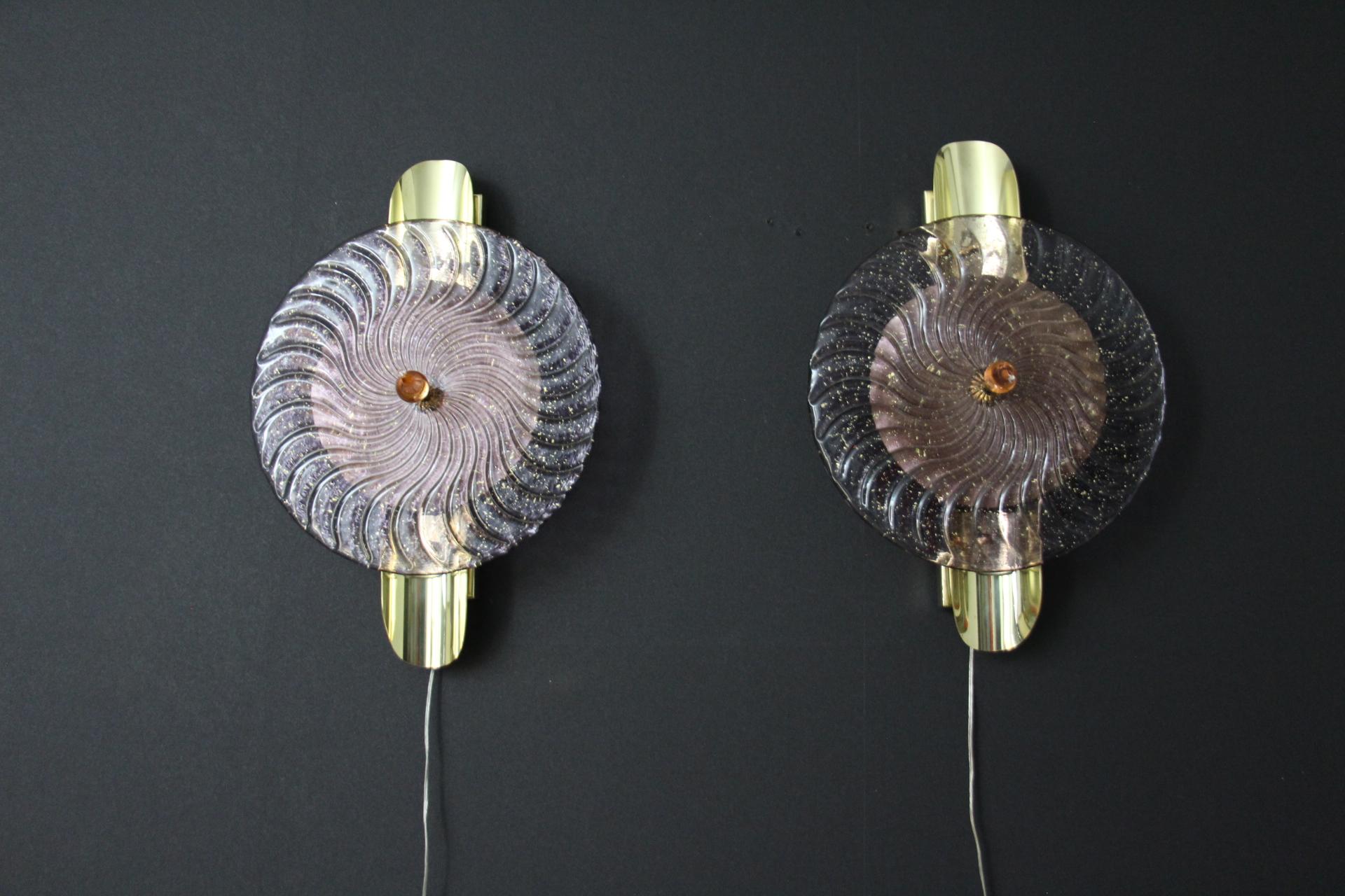 This striking pair of wall lamps is made of textured pink-purple Murano glass disk worked like a spiral swirled, put on a textured brass plate to produce this exceptional effect of changing color between pink, purple and gold . This work of art