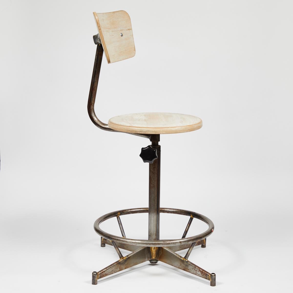 1940s French industrial swivel stool or chair in light blonde wood with adjustable metal base. Featuring a flat circular seat and curved trapezoidal back, the chair sits on a pedestal base with a circular foot-rest and four thin wedge-shaped legs.