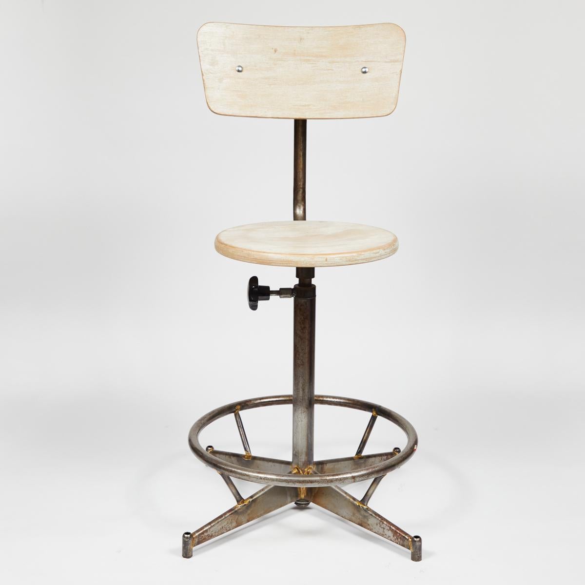 1940s French industrial swivel chair or stool in light blonde wood with adjustable metal base. Featuring a flat circular seat and curved trapezoidal back, the chair sits on a pedestal base with a circular foot-rest and four thin wedge-shaped legs.