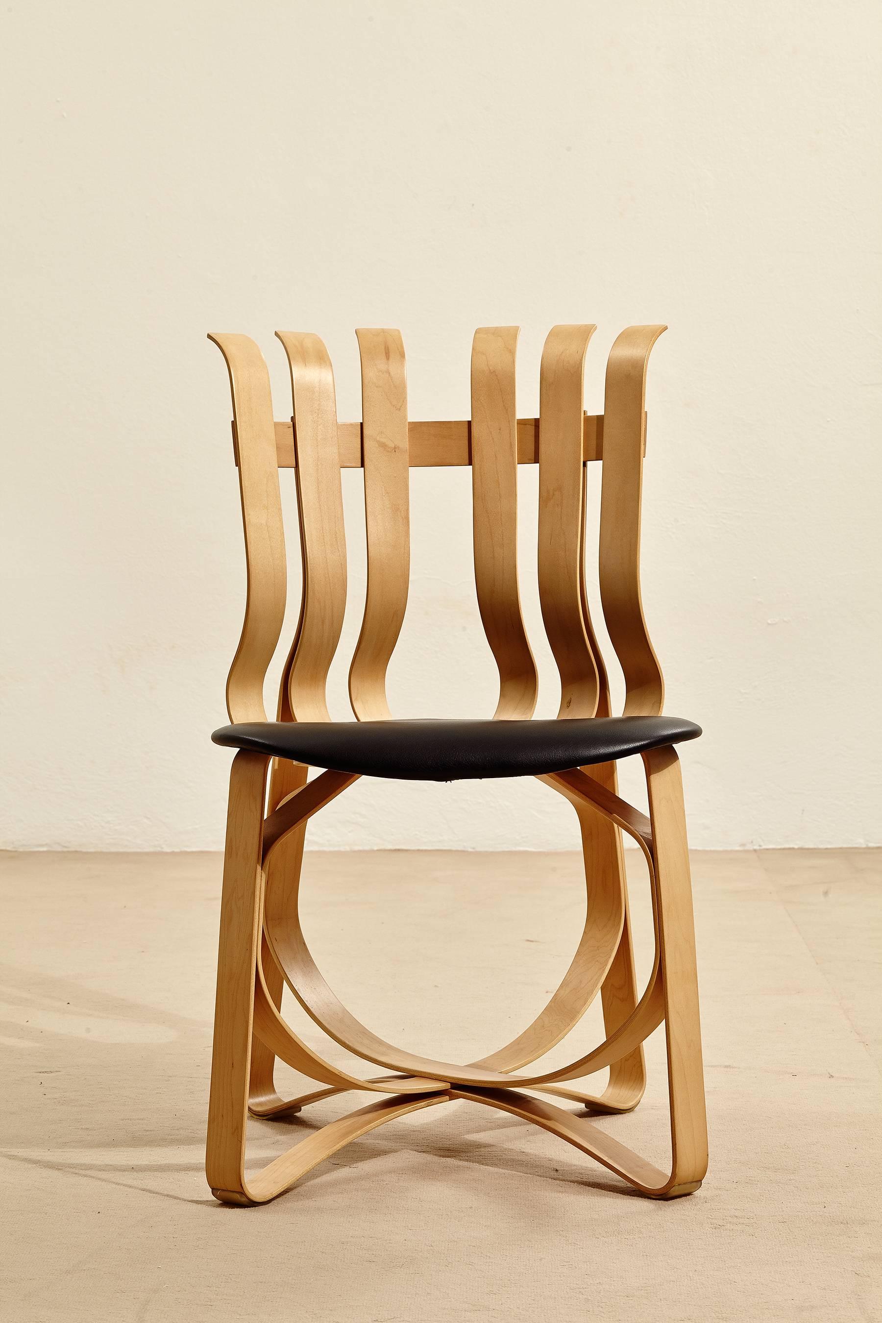 This is an early production of the hat trick chair designed by Frank O. Gehry for Knoll in 1990. The chair is in bent pale maple wood with black leather upholstered seat and is a great example of the architect's sculptural, organic approach to