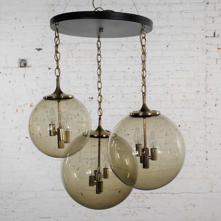 Incredible Lightcraft of California Mid-Century Modern black and brass chandelier or ceiling light with 3 cascading smoke glass orb shaped globes of various sizes. It is in fabulous vintage condition. The brass has been cleaned and you may find