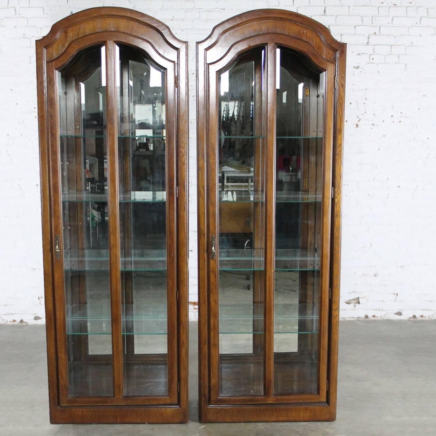 Handsome pair of lighted curio cabinets or vitrines in a beautiful dark wood with arched tops and mirrored inside backs. These cabinets are in wonderful vintage condition, circa 1980s-1990s.

Just what the designer ordered! A pair of interesting