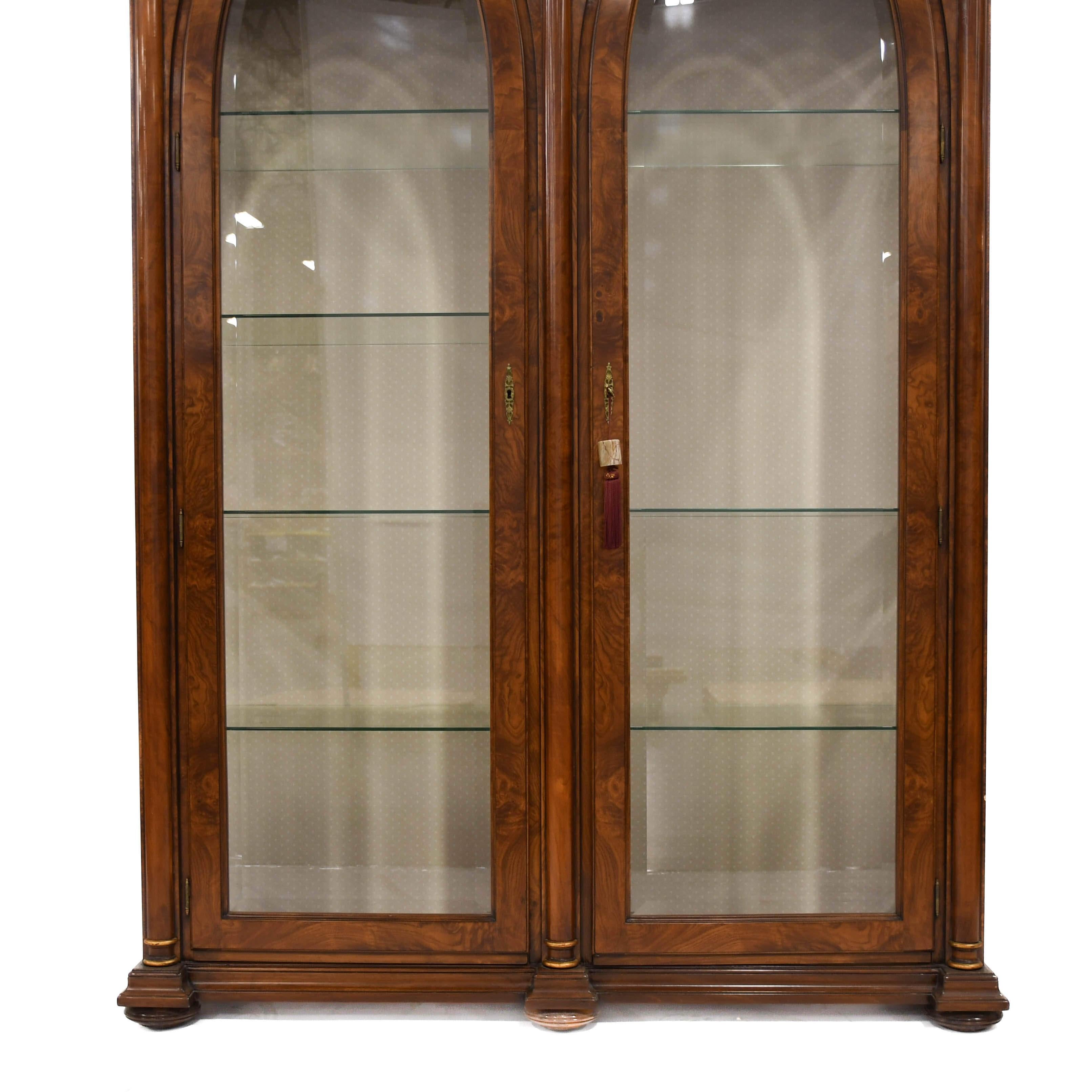 Questa libreria in noce a due ante in vetro con colonne corinzie presenta una ricca finitura in noce, due ante in vetro per una maggiore visibilità e colonne corinzie decorate con capitelli dettagliati. Offre ripiani regolabili per libri o oggetti