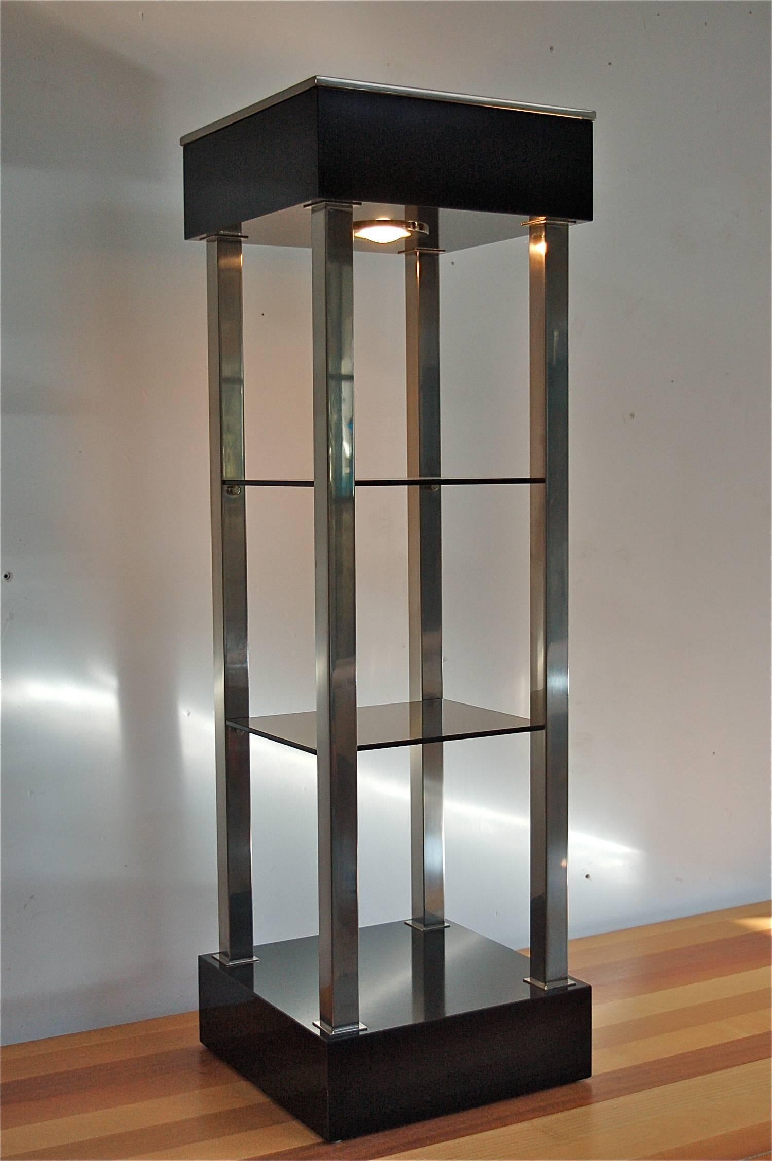 1970s retro shop or tower display case with top lighting by quality Belgian manufacturer Belgo Chrome. The square base and top are made of black lacquered wood. The top has a built in light fixture, a down lighter. It has four polished metal pillars