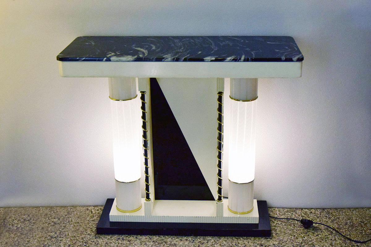 Lighting console, Italian production from the 1970s.
Painted wooden structure with luminous columns in reeded Murano glass, top in black Marquinia marble and golden details.
In excellent condition.