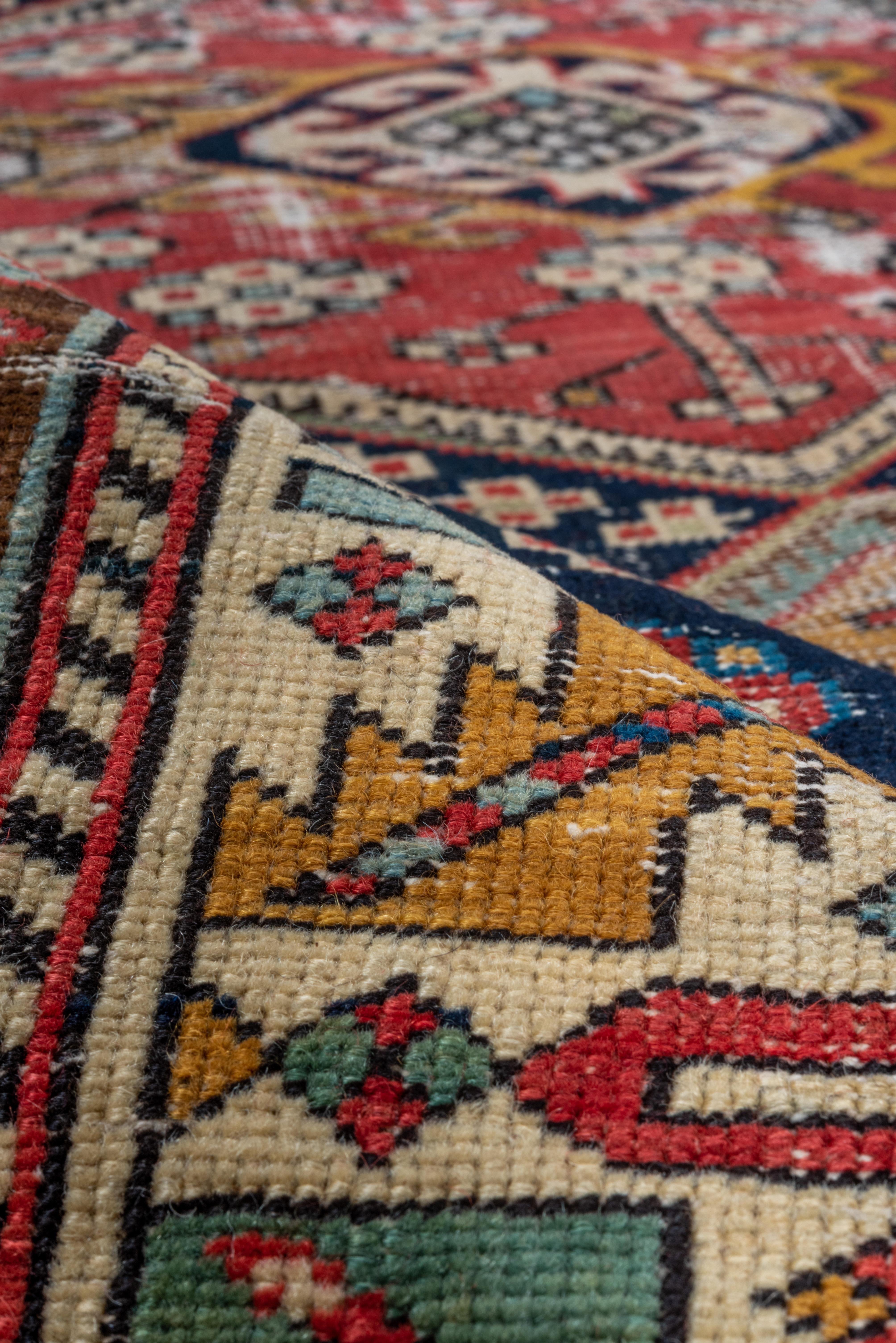 Dieser lange Teppich im Shabby-Chic-Stil hat trotz seiner Abrasion einen echten Charakter. Das marineblaue Feld zeigt ein Stabmedaillon aus drei abgeflachten Sechsecken in Rot, Hellblau, Blassblau und Goldrute, die hakenförmige Rauten oder Rechtecke