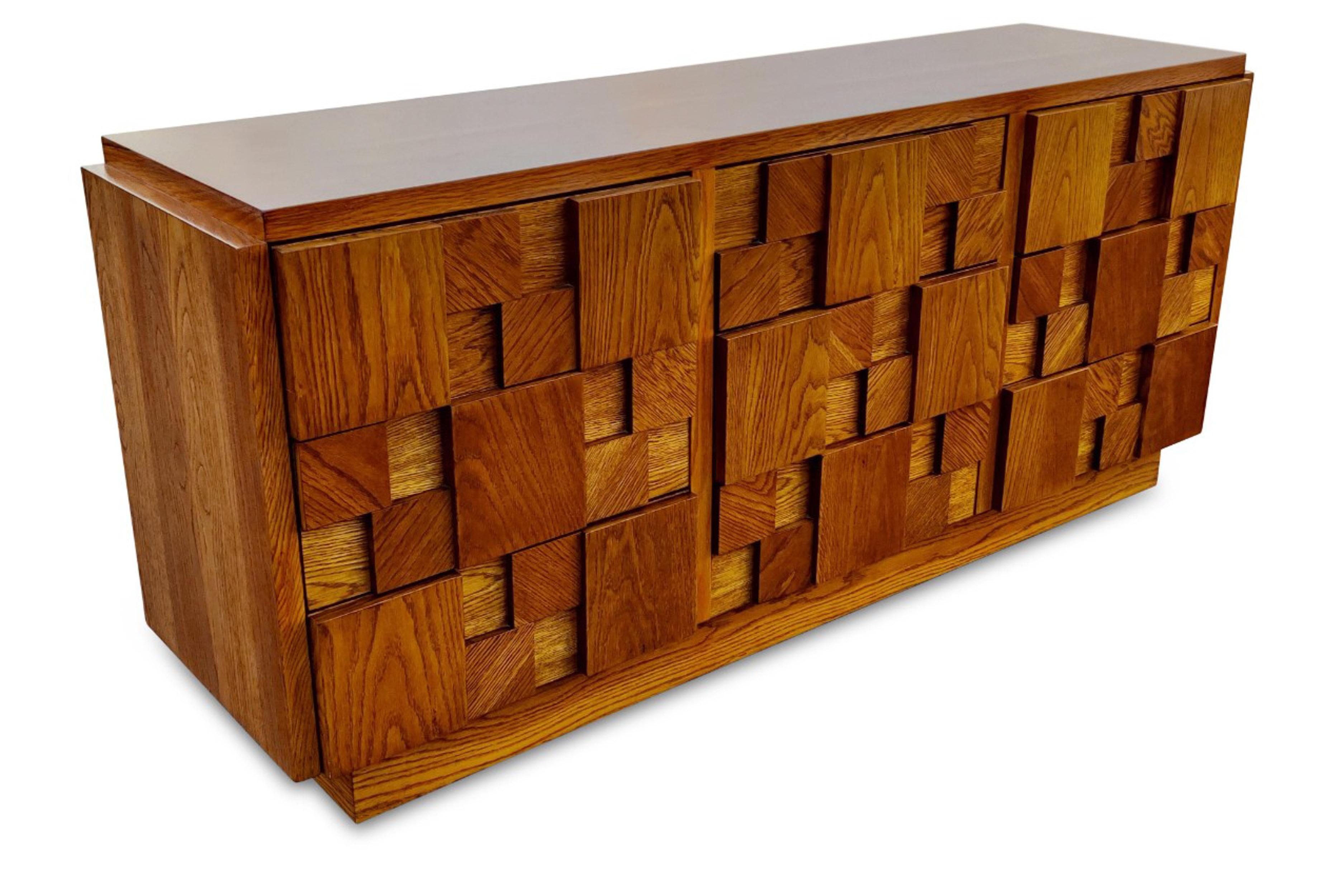 This dresser was designed in the brutalist style made iconic by Paul Evans, and manufactured by Lane USA, circa 1970s. Made with varied blocks of oak attached to the front, it lends an imposing and dramatic look while retaining the rich color and