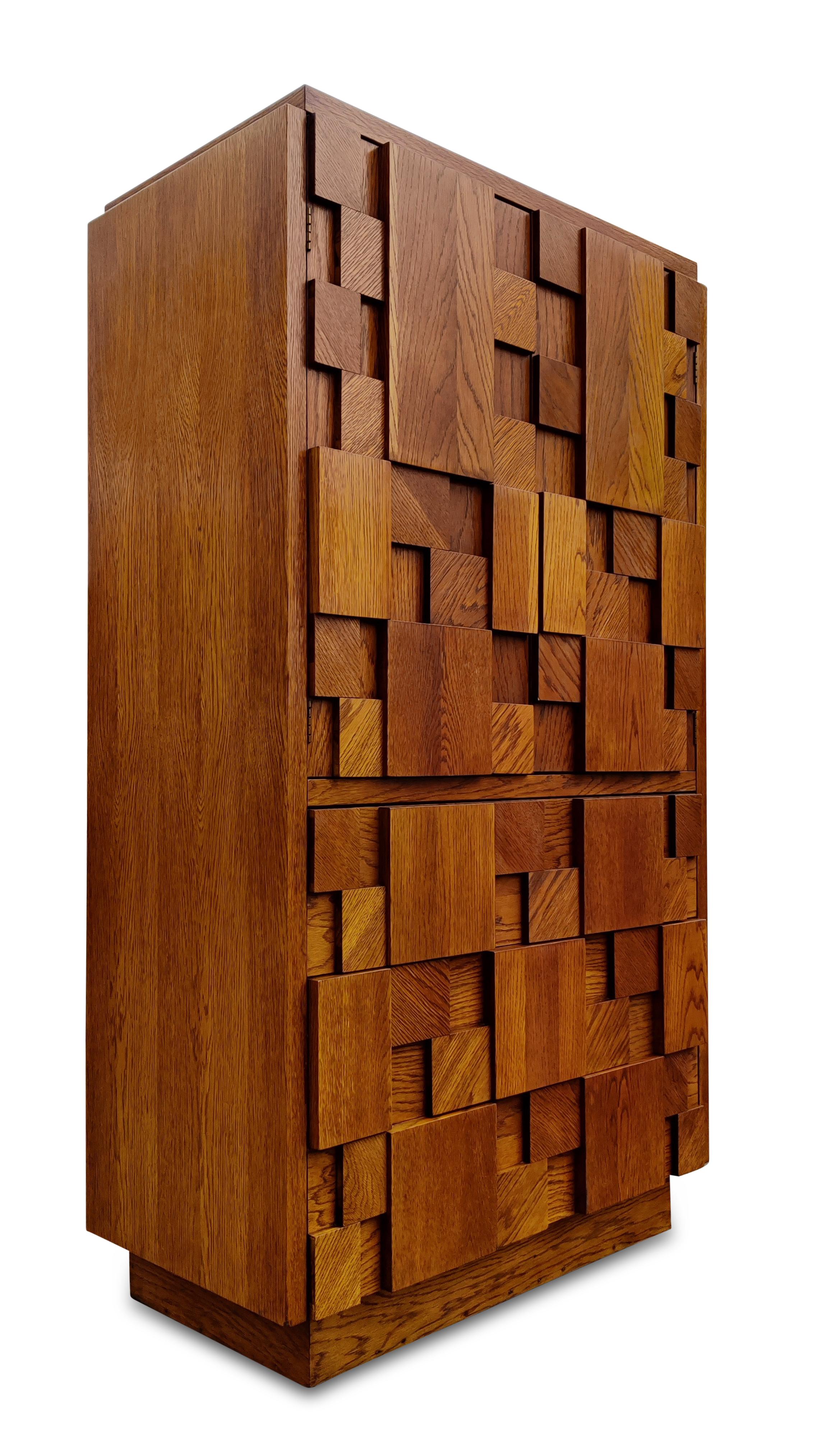 This tall chest was designed in the brutalist style made iconic by Paul Evans, and manufactured by Lane USA, circa 1970s. Made with varied blocks of oak attached to the front, it lends an imposing and dramatic look while retaining the rich color and
