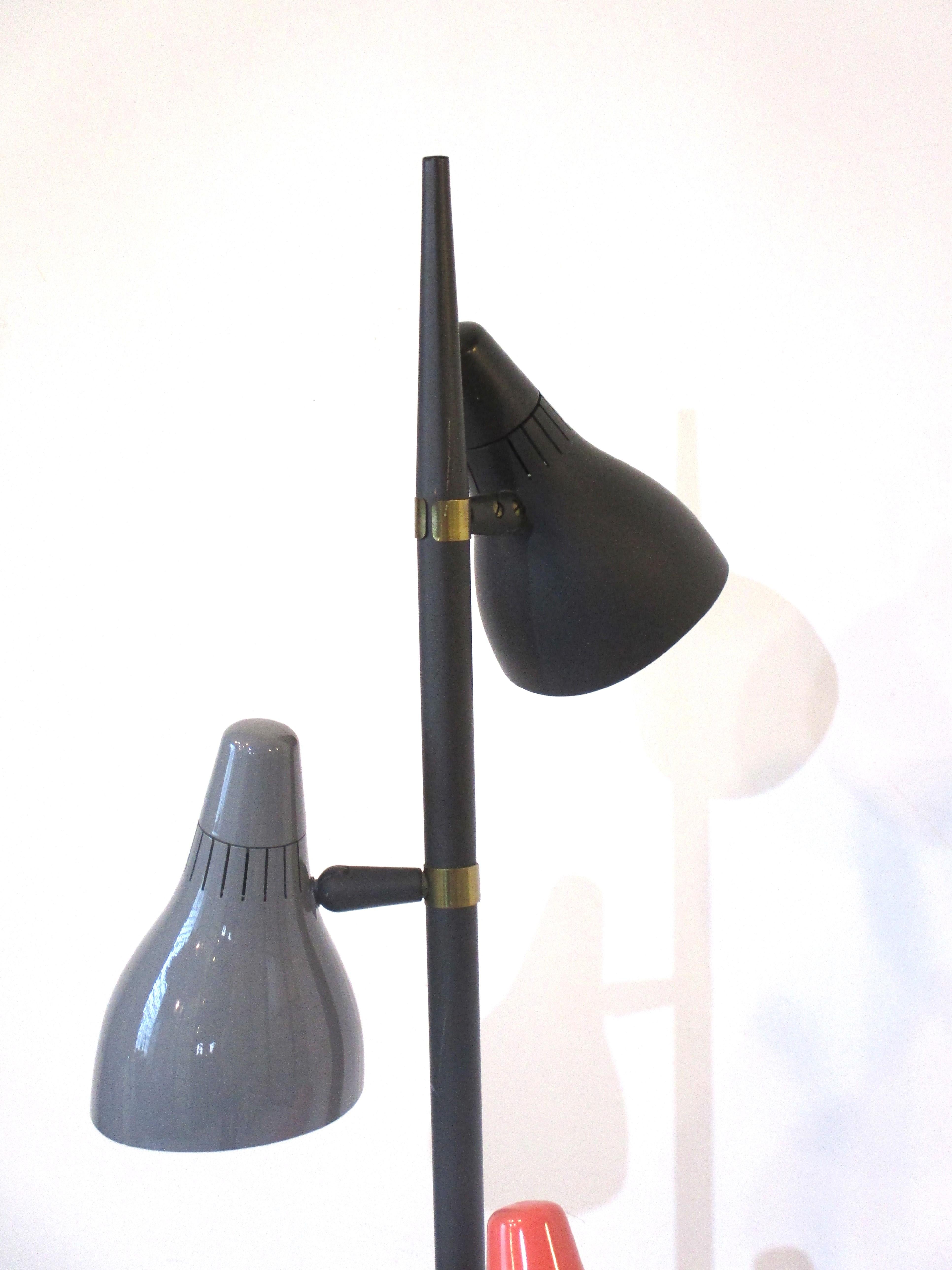 A three headed adjustable Mid Century pole floor lamp with a black, gray and coral plastic shade. The metal pole is in a satin black with round base having a brass ring detail, each lamps rounded top point is a twist and turn type switch.