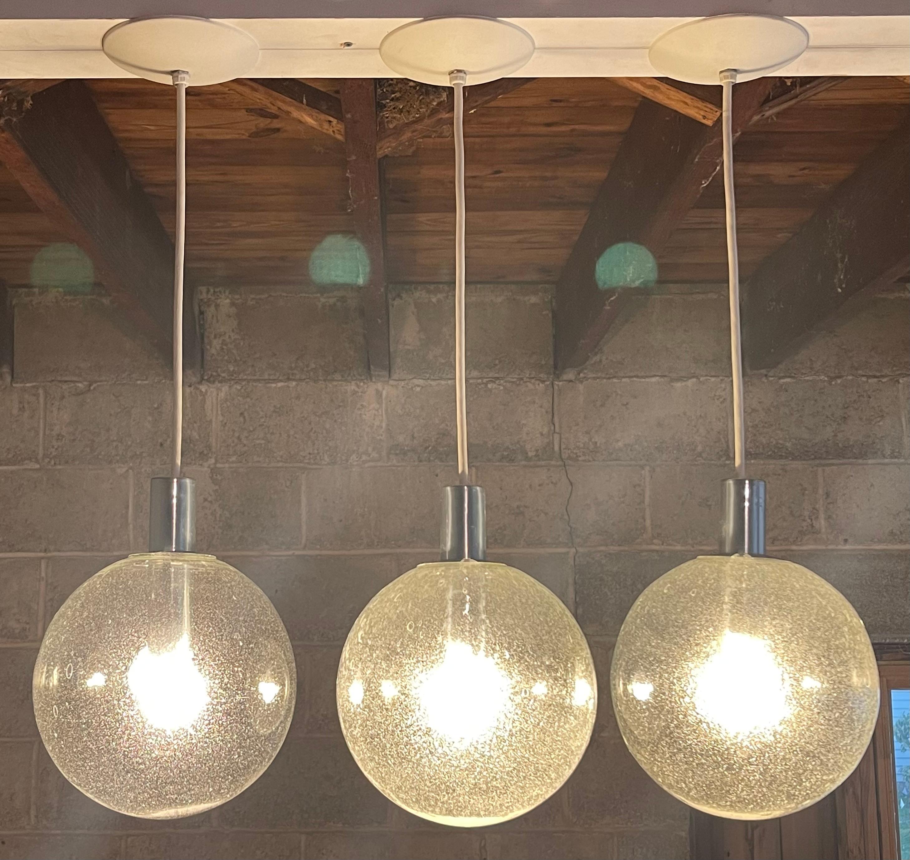 Lightolier pendant lamps executed in pulegoso glass. Signed twice with manufacturer's sticker to chrome hardware and canopy of each fixture. Please note that due to the handmade nature of the glass, one of the three globes reads as more transparent