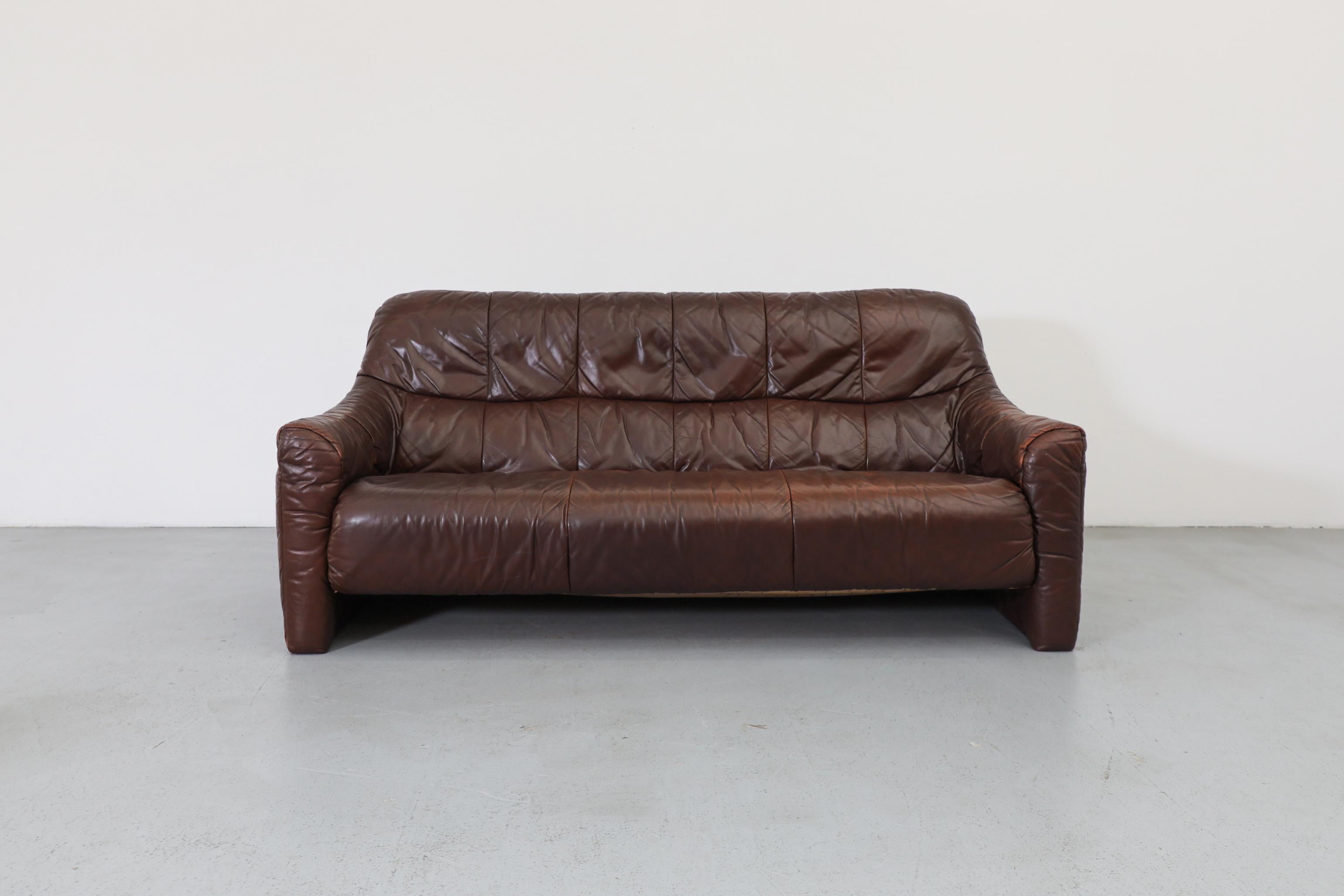 A handsome Mid-Century chocolate brown leather loveseat in the style of Ligne Roset. This low-profile sofa channels relaxed luxury with its soft lines, gentle curves, and elegant pleating, offering excellent comfort with a built-in lumbar cushion.