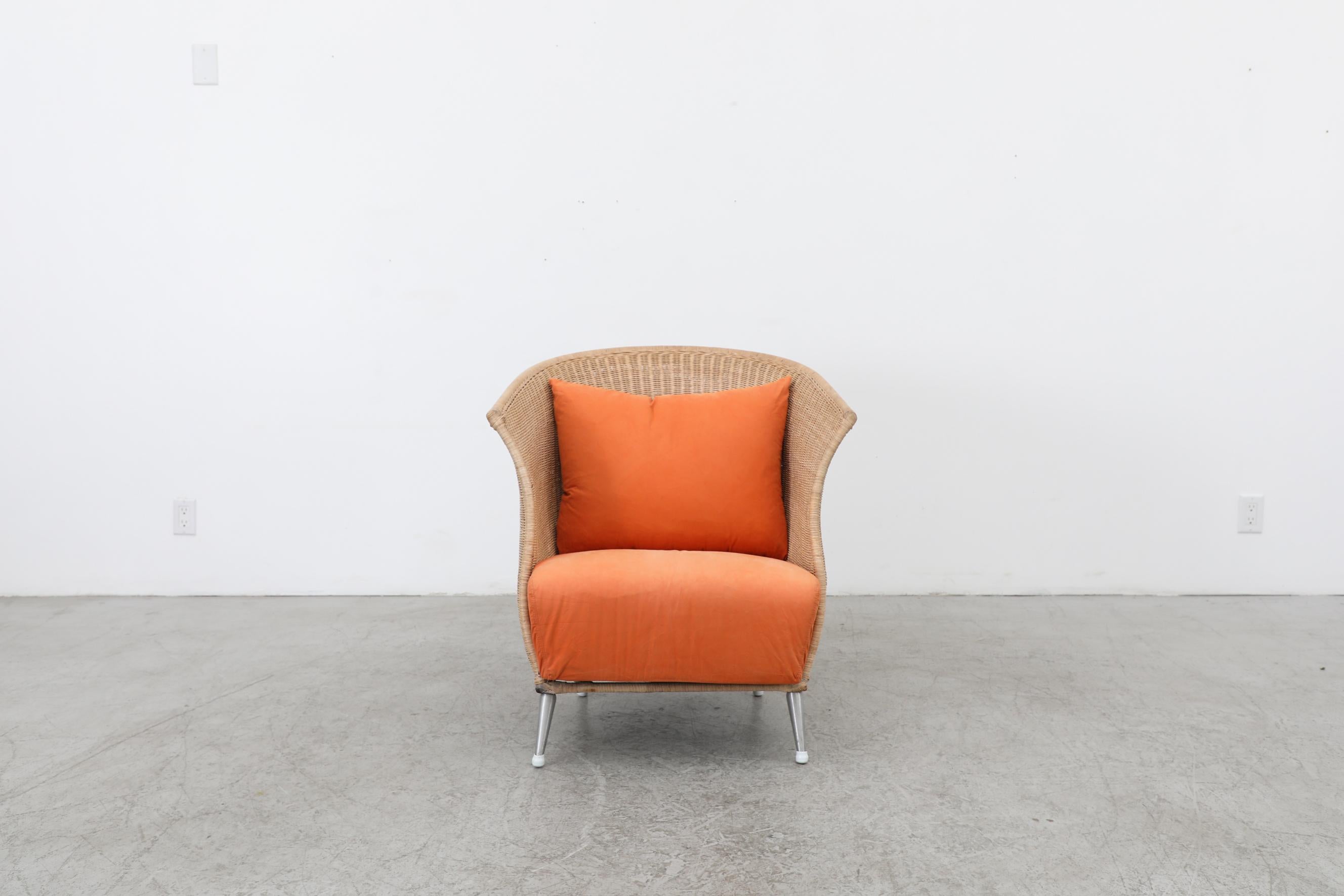 Ligne Roset rattan lounge chair with orange cushion. In original condition with normal wear for its age and use. There is some rattan breakage on the back and fading to the rattan on the interior. The seat width is 22.5