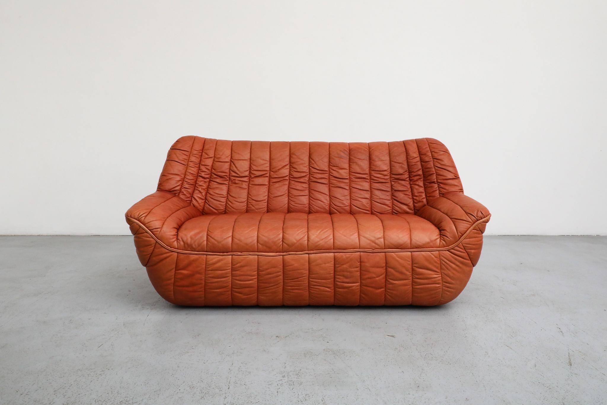 A stunning soft-form leather loveseat with distinctive ribbed, linear-quilted upholstery, skillfully crafted in the 1970s by Germany's Laauser company. This exceptionally comfortable sofa draws direct inspiration from the iconic designs of Annie