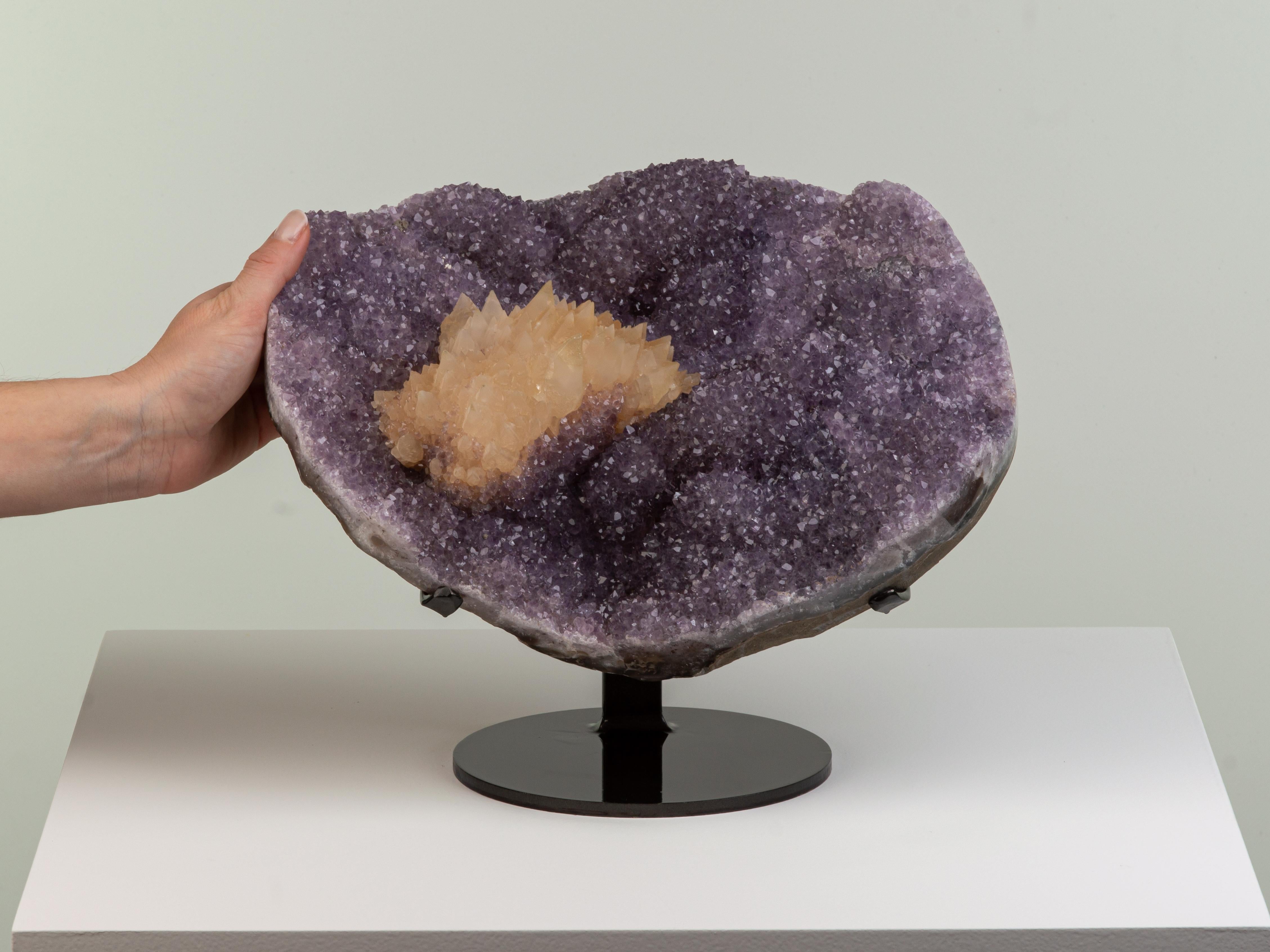 A large bowl shaped piece formed of small lilac amethyst crystals with a
stunning central honey coloured calcite formation resembling a rosette.
At the base of the calcite pink druzy quartz can be seen.

This piece was legally and ethically