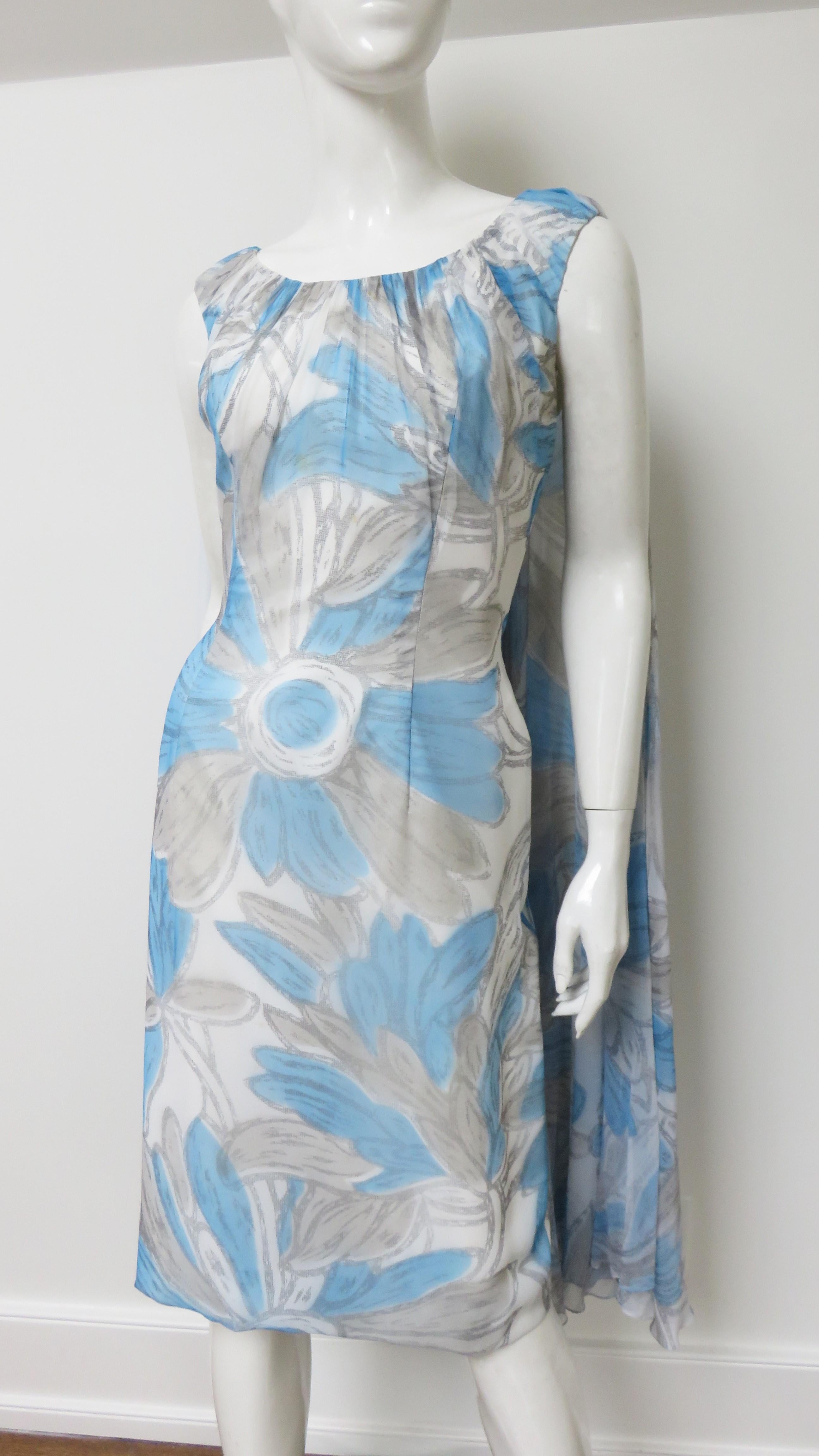 A beautiful white, grey and blue abstract flower pattern silk dress from Lilli Diamond. It is sleeveless, semi fitted with a gathered crew neckline and back drapery the length of the dress. It is fully lined and has a back zipper. Unworn with inner