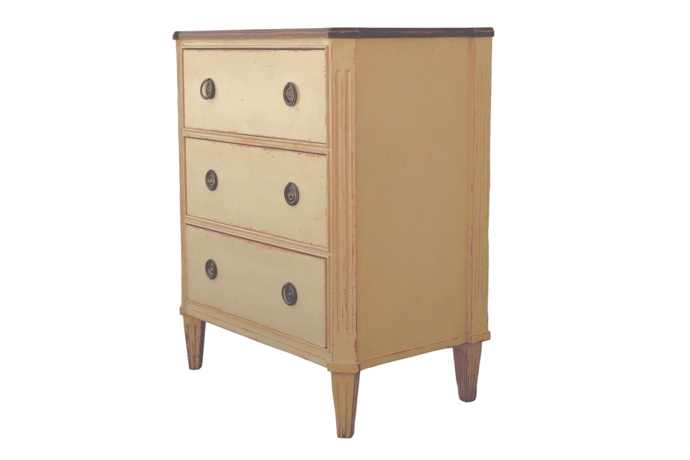 A Lillian August small bureau. Three hand dovetailed drawers open with round metal handles against round beveled backplates. The top drawer is separated into three compartments, and angled fluted corners flank the drawers, giving the piece a French