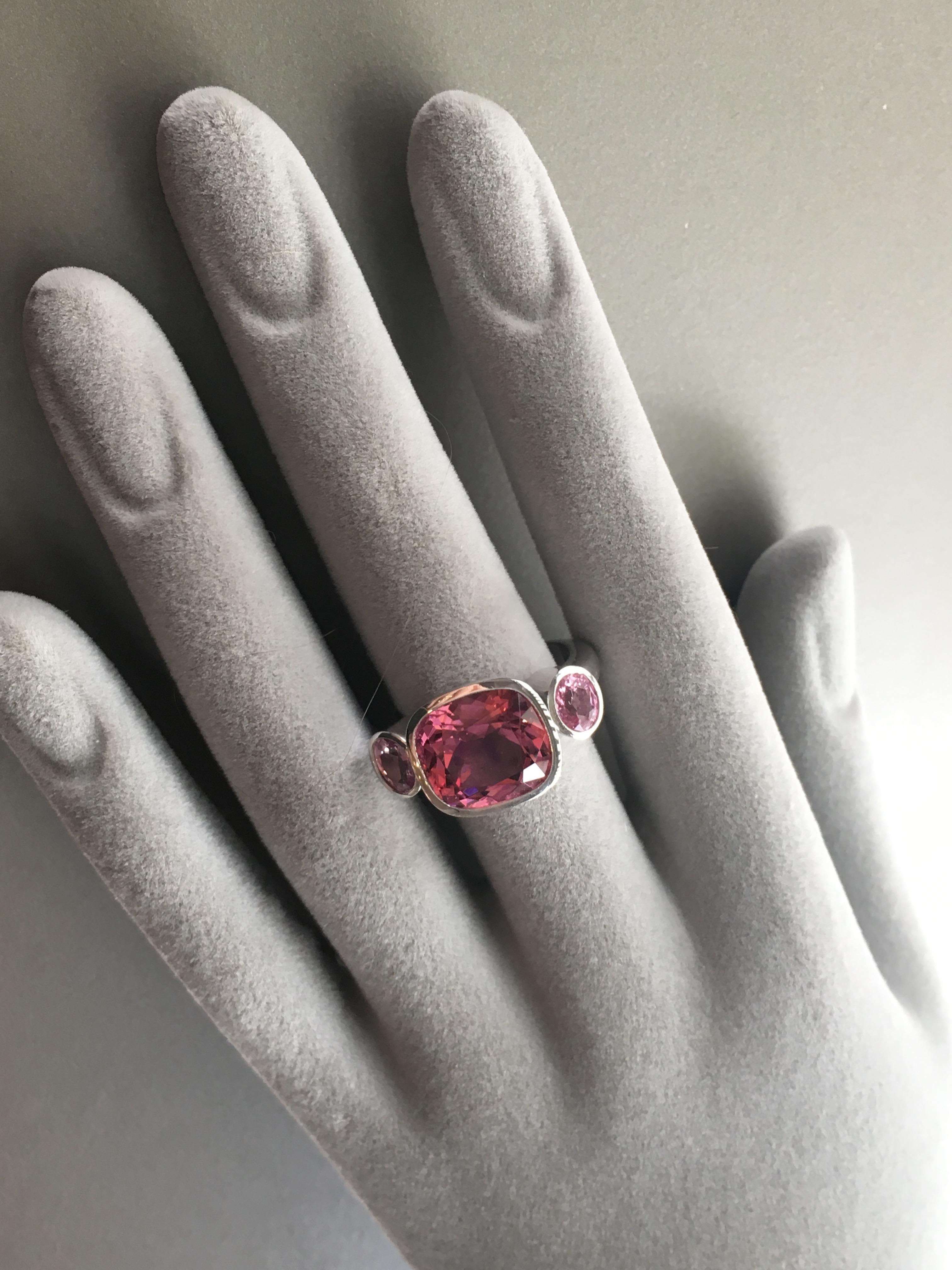A stunning three stone ring with a  pink tourmaline cushion in the center and a pair of Padparascha oval sapphires on either side. The ring is set in 18 Karat white gold.
It can be used as a day ring or as a cocktail ring.  It would also make a