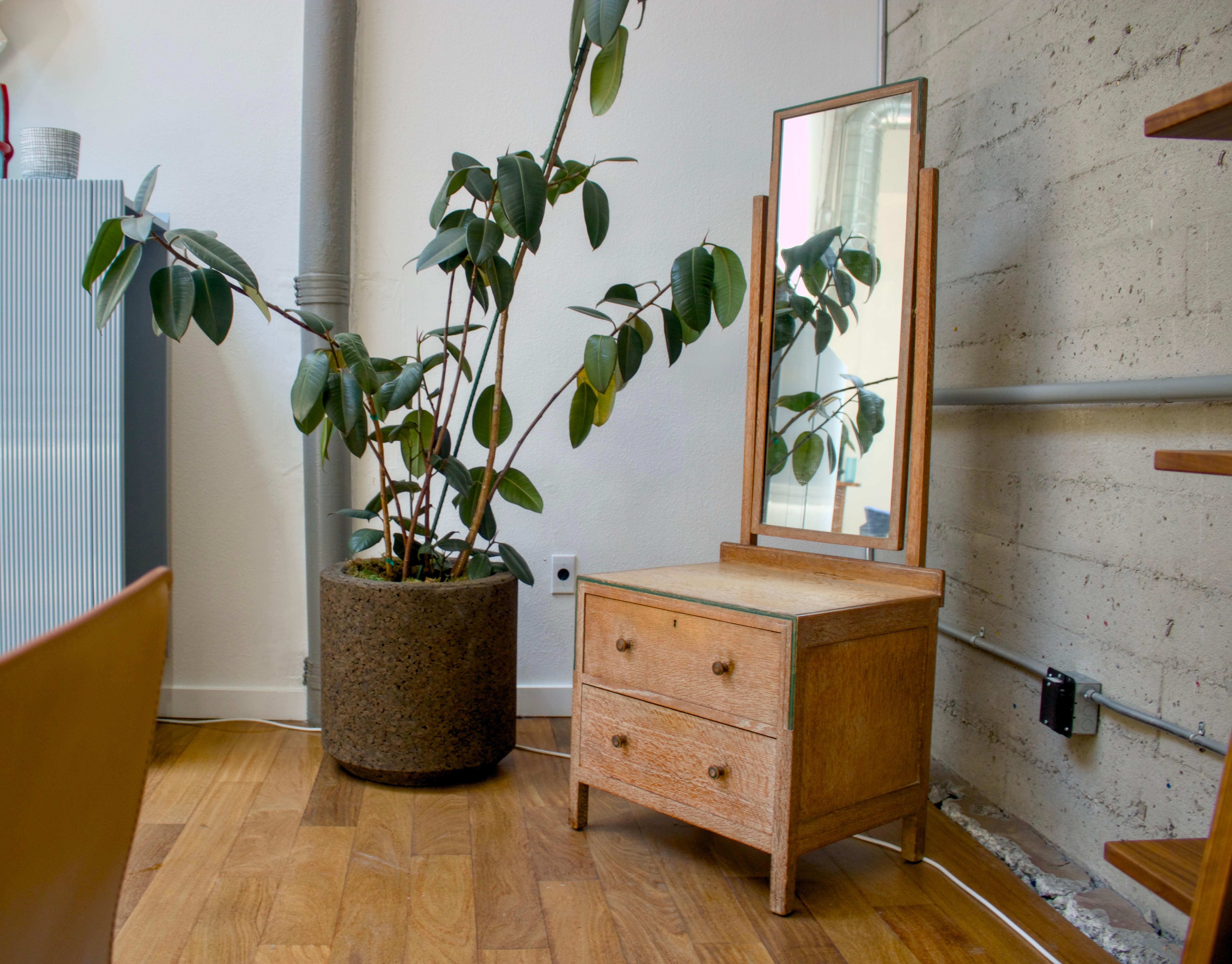 A limed oak chest of drawers with mirror, made by Heals of London, circa 1930. It consists of two spacious drawers (6.75” H x 21.25” W x 16.25” D) with detachable swivel mirror (39” H x 16” W). In total, it is 65” tall with a base measuring 24” H x