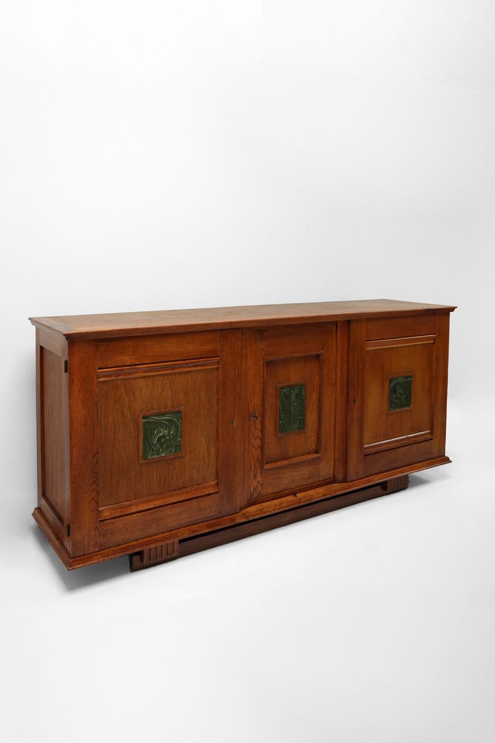 Limed oak sideboard opening with three front doors, each decorated with a blackened carved wooden tile with an animal motif France, 1940s.