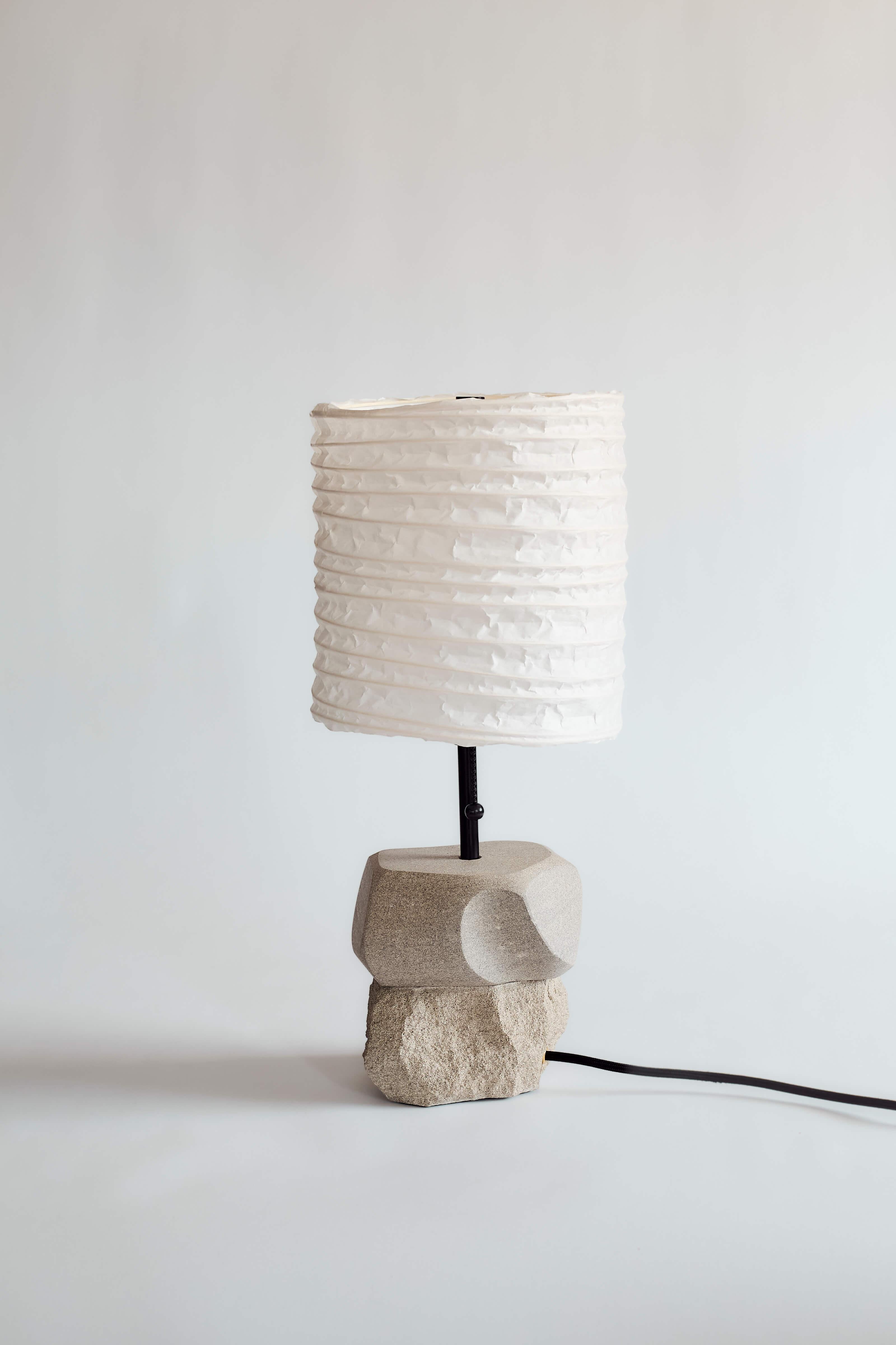 The result of a gestural movement practice, the ribboning shapes and hard edges carved into the stone invite touch. Each abstract piece is a conversation between play, severity and high craft. The handmade lampshade glows warmly, welcoming it as