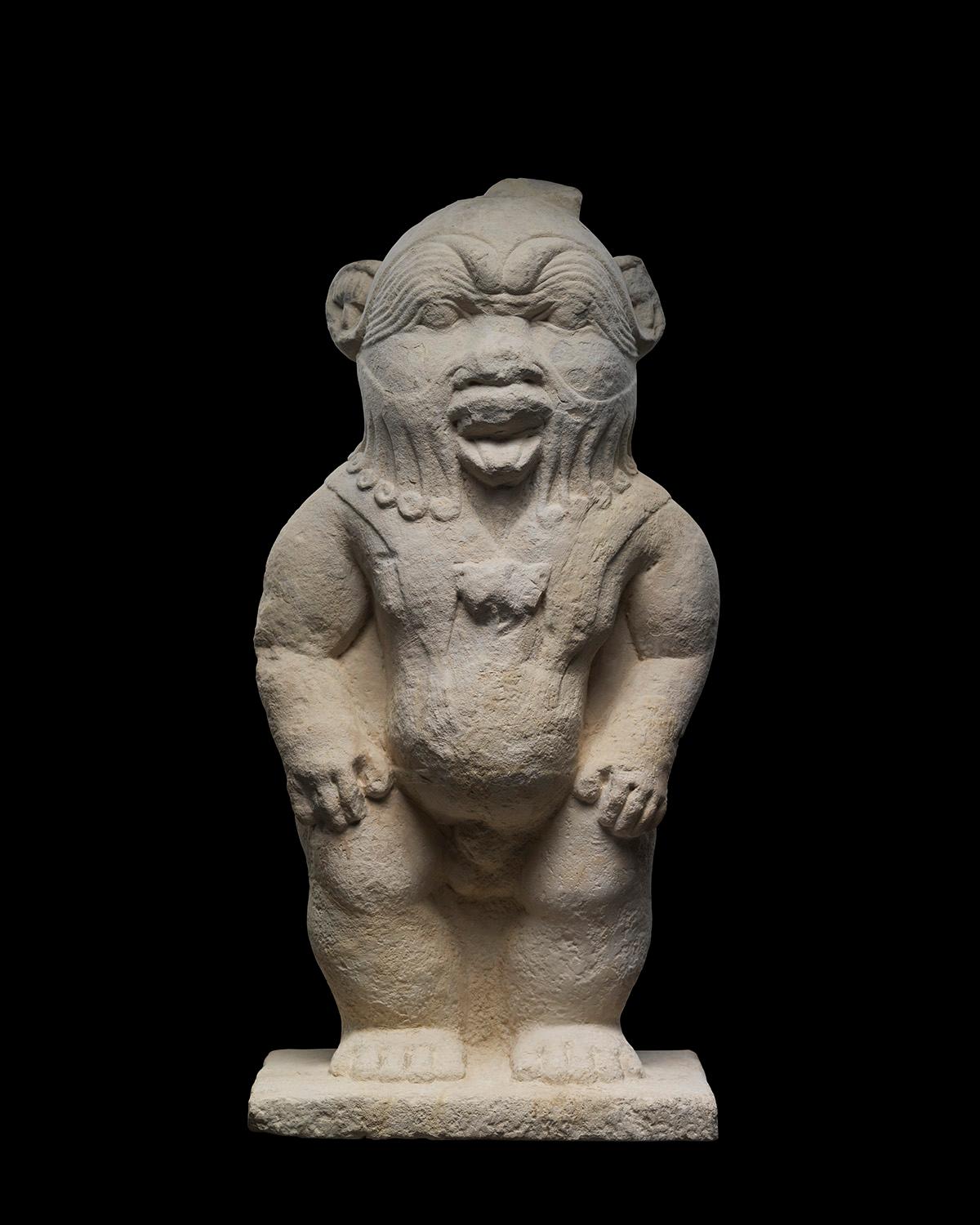 Una grande statua indipendente dell'antico dio egizio Bes nella sua forma canonica di nano tarchiato. Il suo viso è molto espressivo, con grandi sopracciglia a goccia disegnate in un cipiglio esagerato sugli occhi piccoli e profondi. Grandi orecchie