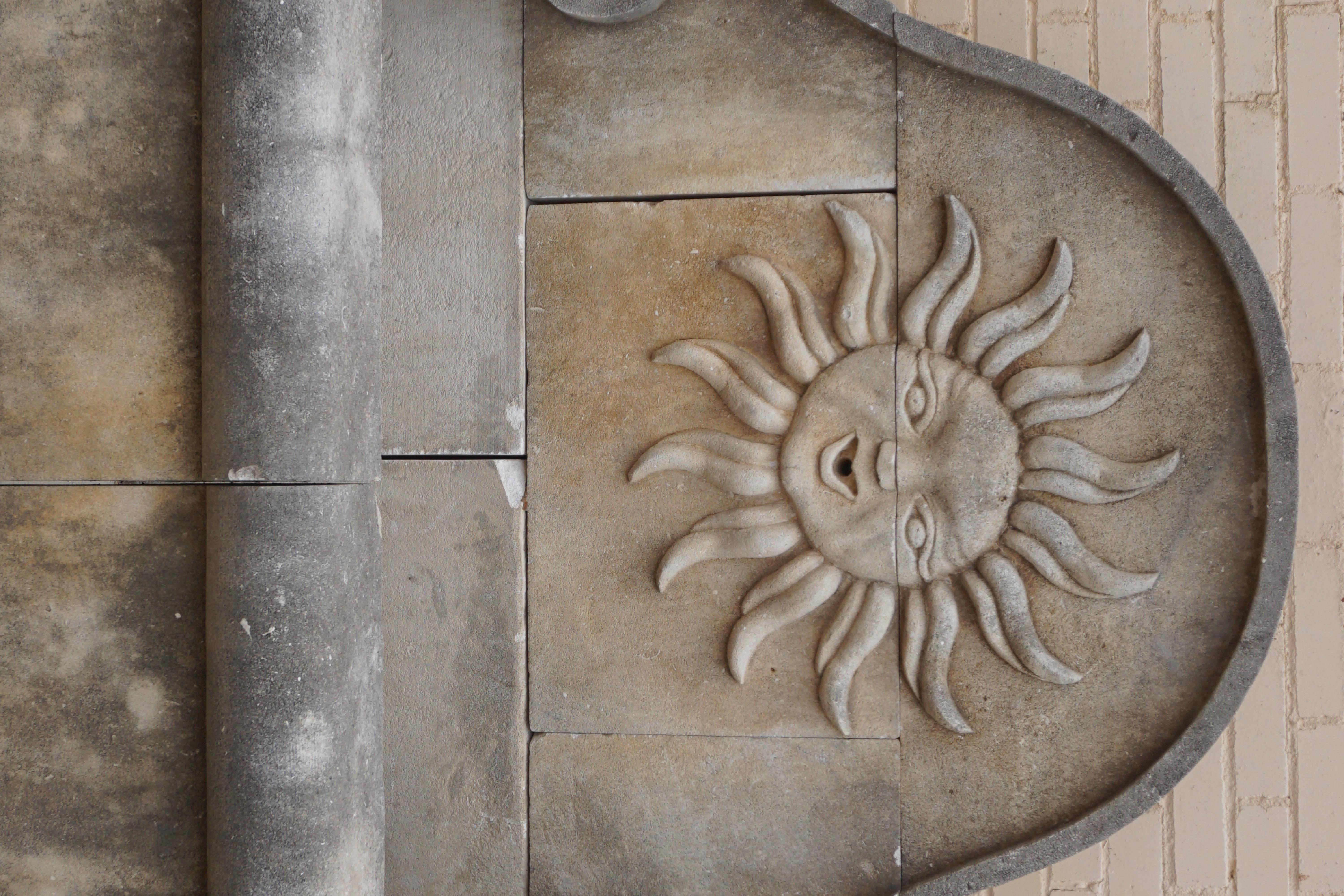 Fontaine murale en pierre calcaire sculptée à la main, avec une sculpture centrale du soleil et un visage humain sur la plaque arrière. Inspiré par Louis XIV, qui avait choisi le soleil comme emblème, ce symbole était lié à Apollo, le dieu de la